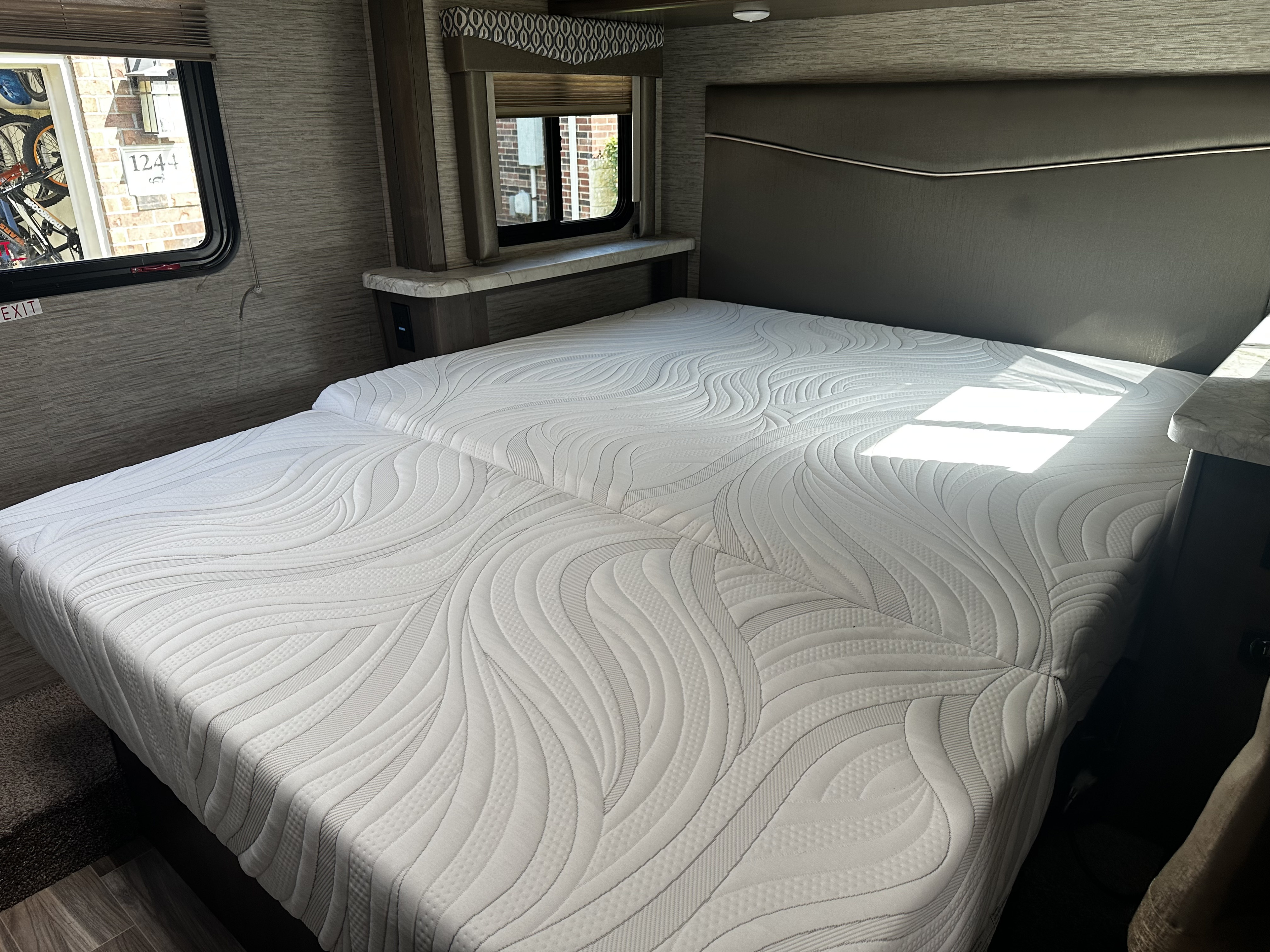 RV rental interior: A cozy bedroom featuring two mattresses forming a bed, with a window view of house #1244 and bicycles.. Thor Freedom Elite 2021