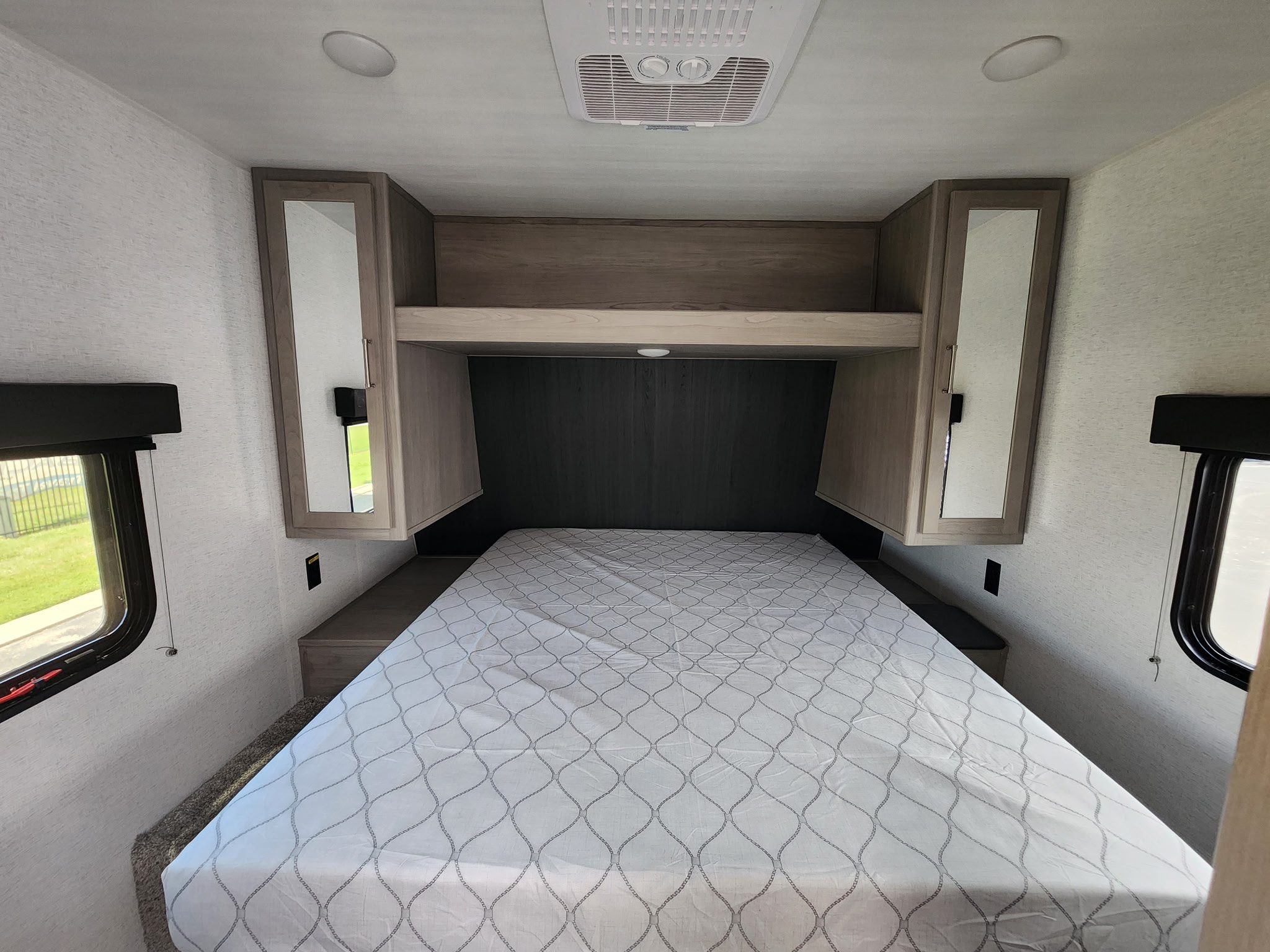 Modern RV rental bedroom with bed, overhead storage, mirrored cabinets, windows & ceiling AC.. Keystone RV Springdale 25th Anniversary 2024