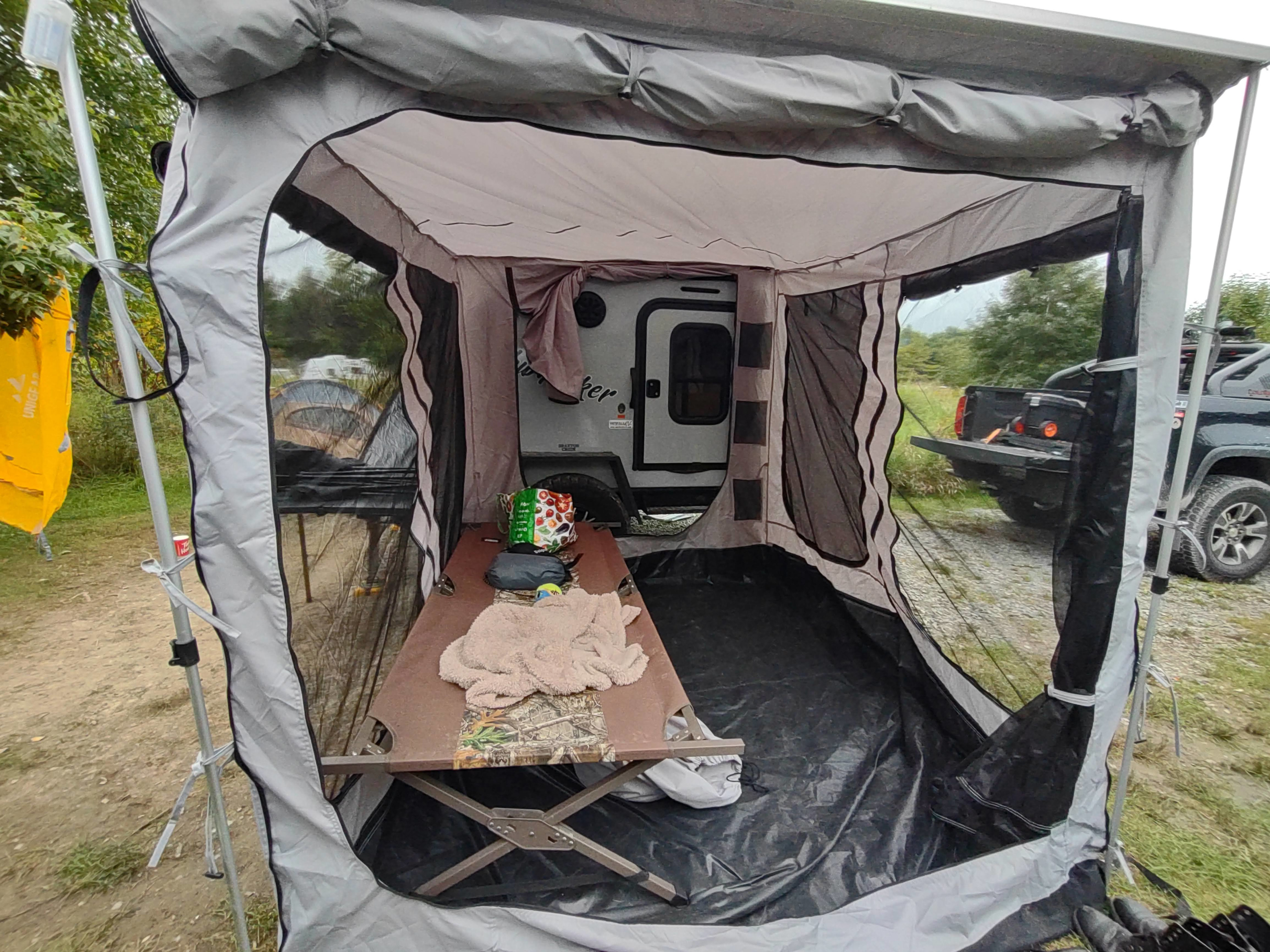 Inside a spacious tent attached to a small camper, featuring a cot and ground tarp, ideal for an RV rental trip.. Braxton Creek Bushwhacker 2023