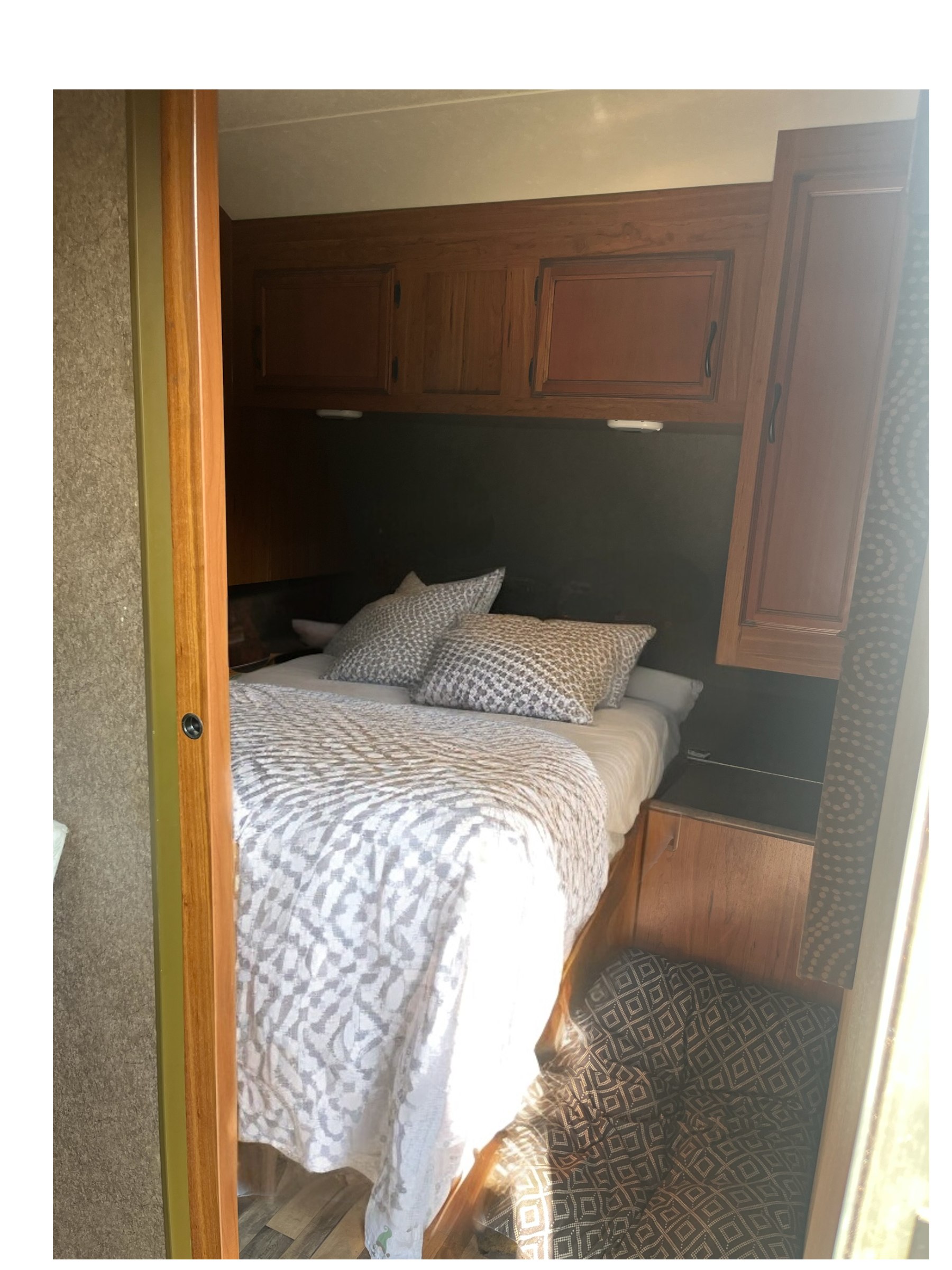 Cozy RV rental bedroom featuring patterned bedding, overhead wood cabinets, and compact design for comfortable travel accommodation.. Starcraft Autumn Ridge 2015