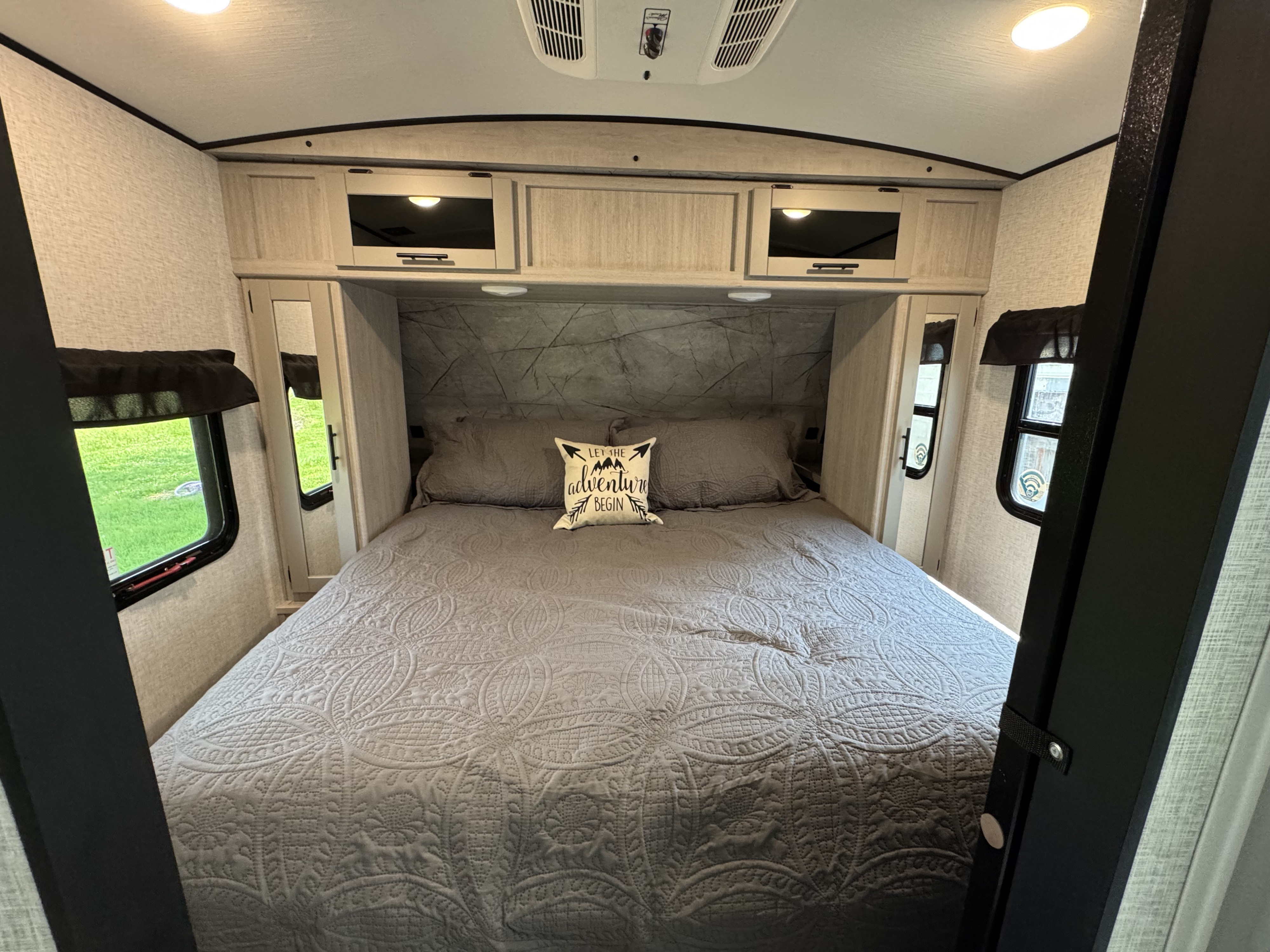 This comfortable RV rental bedroom features a queen bed, storage, and an "adventure" pillow, ideal for road trips.. Crossroads RV Sunset Trail 2024
