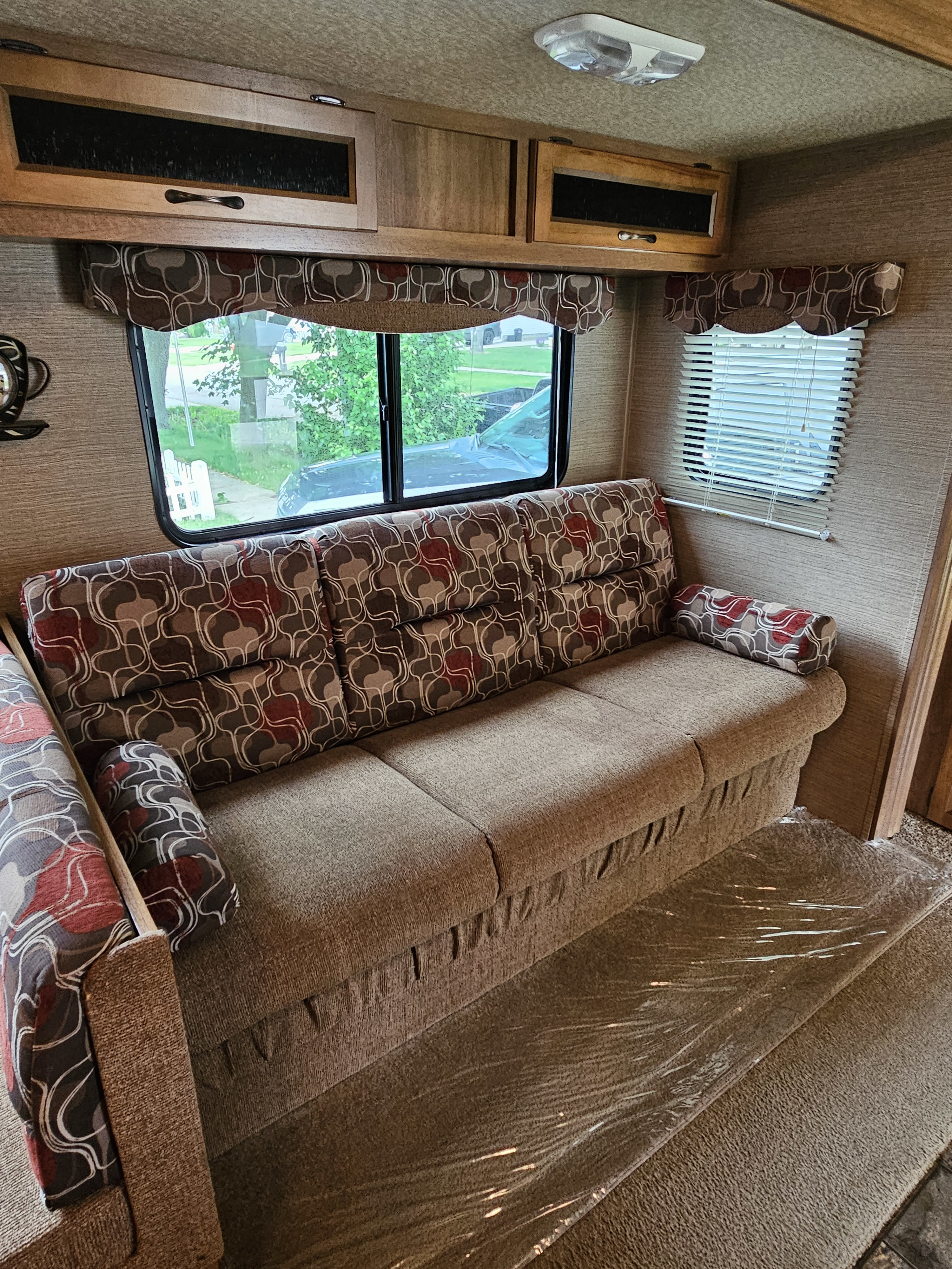 Cozy RV rental interior with patterned sofa, large windows, overhead storage, and carpet protected by film.. Forest River Coachmen Catalina 2014