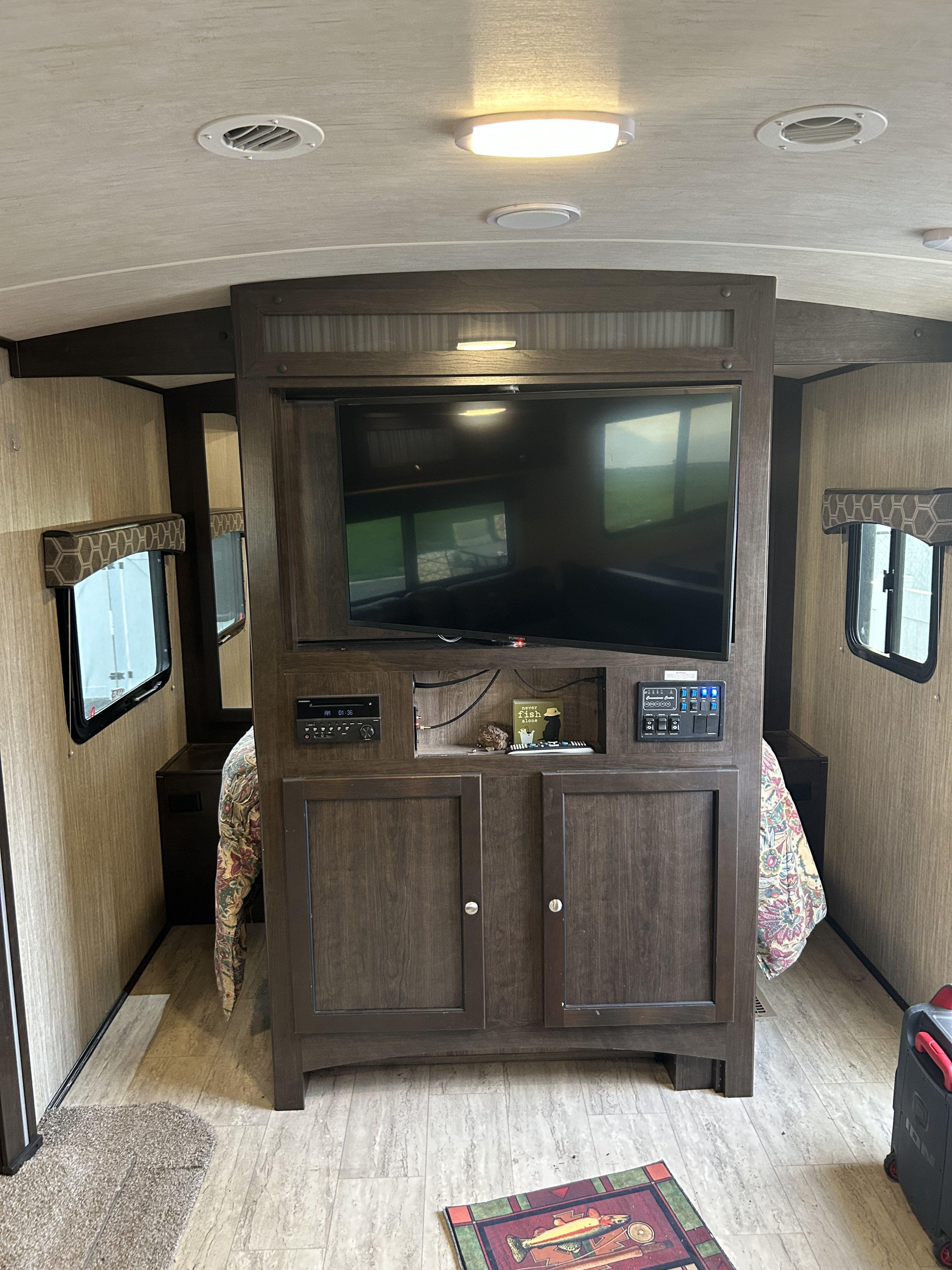 RV rental bedroom with central entertainment: a large TV, stereo system, and functional control panel in a modern wooden unit.. Cruiser RV Shadow Cruiser 2018