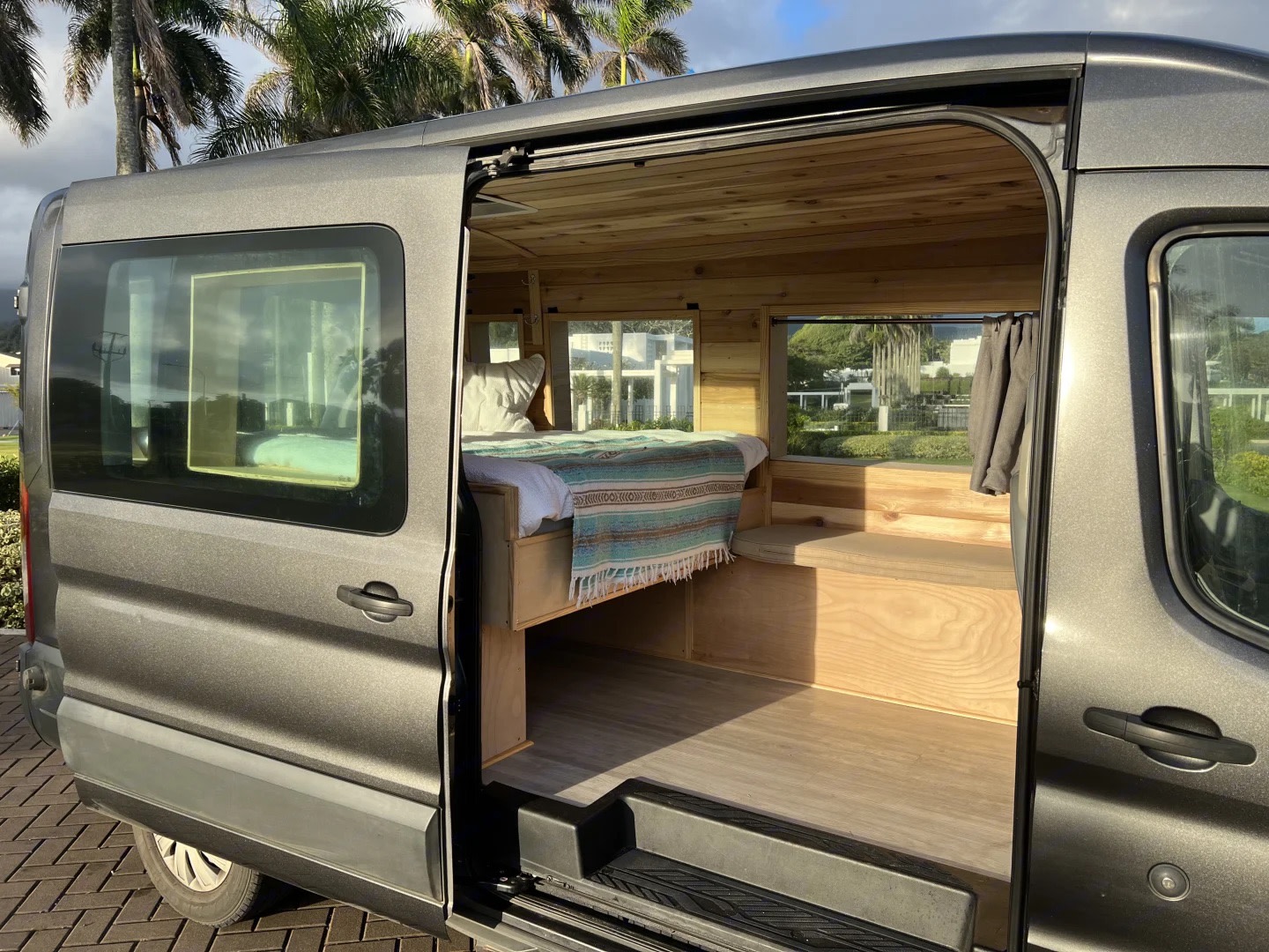 Gray rv rental camper van with open door revealing a custom wood interior, comfy bed, and bright windows for travel.. Ford Transit 2016