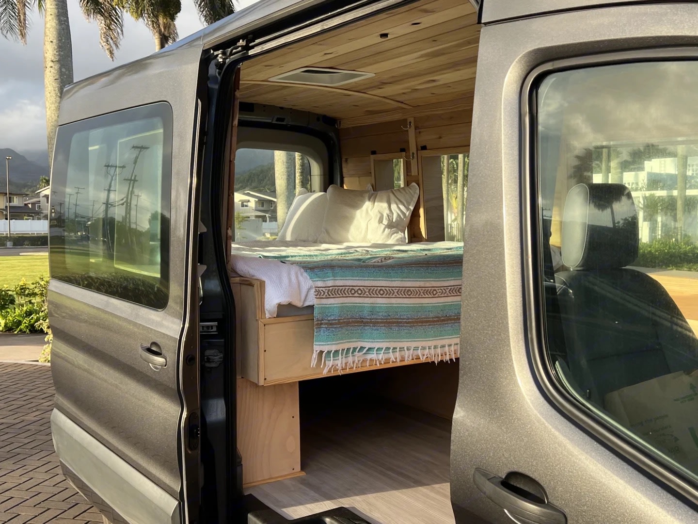 RV rental: A custom grey camper van with its side door open, revealing a cozy bed and warm wooden interior, ready for travel.. Ford Transit 2016