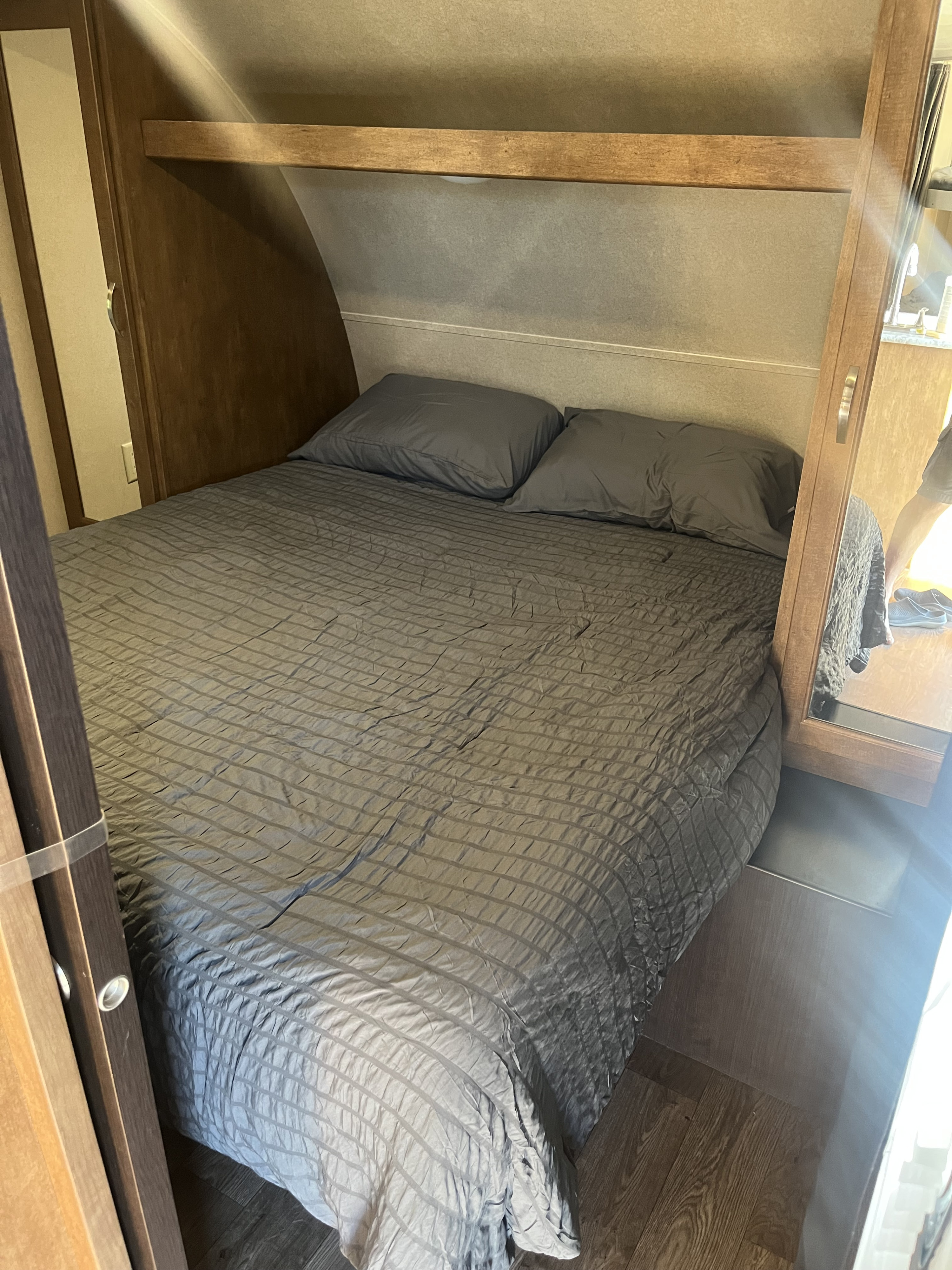 Inside an RV rental: a compact bedroom with a gray-quilted bed, two pillows, and an overhead wooden shelf.. Forest River Salem Cruise Lite 2018