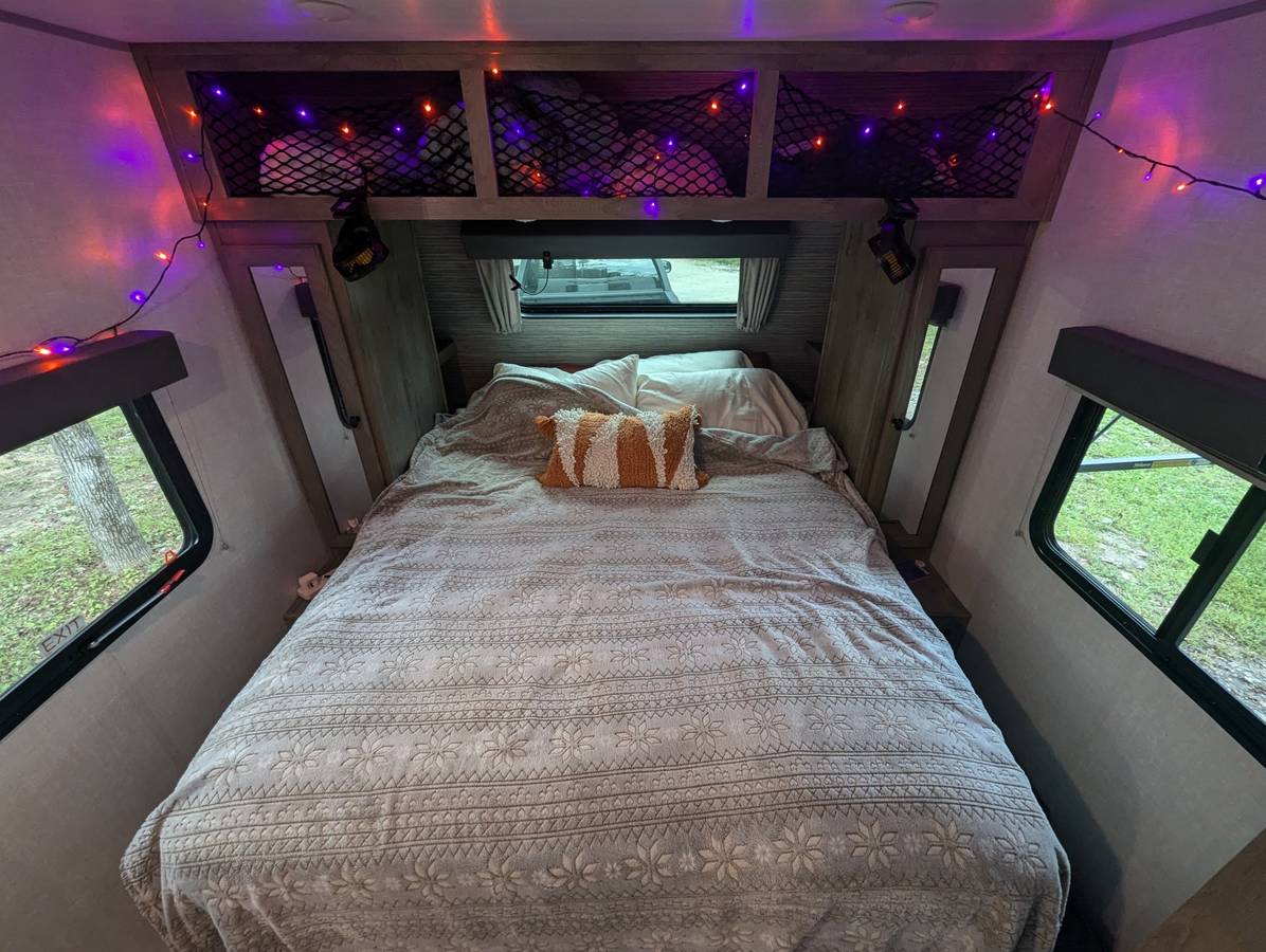 Cozy RV rental bedroom featuring a comfy bed, festive string lights, and scenic outdoor views from the windows.. Forest River Surveyor Legend 19RBLE 2022
