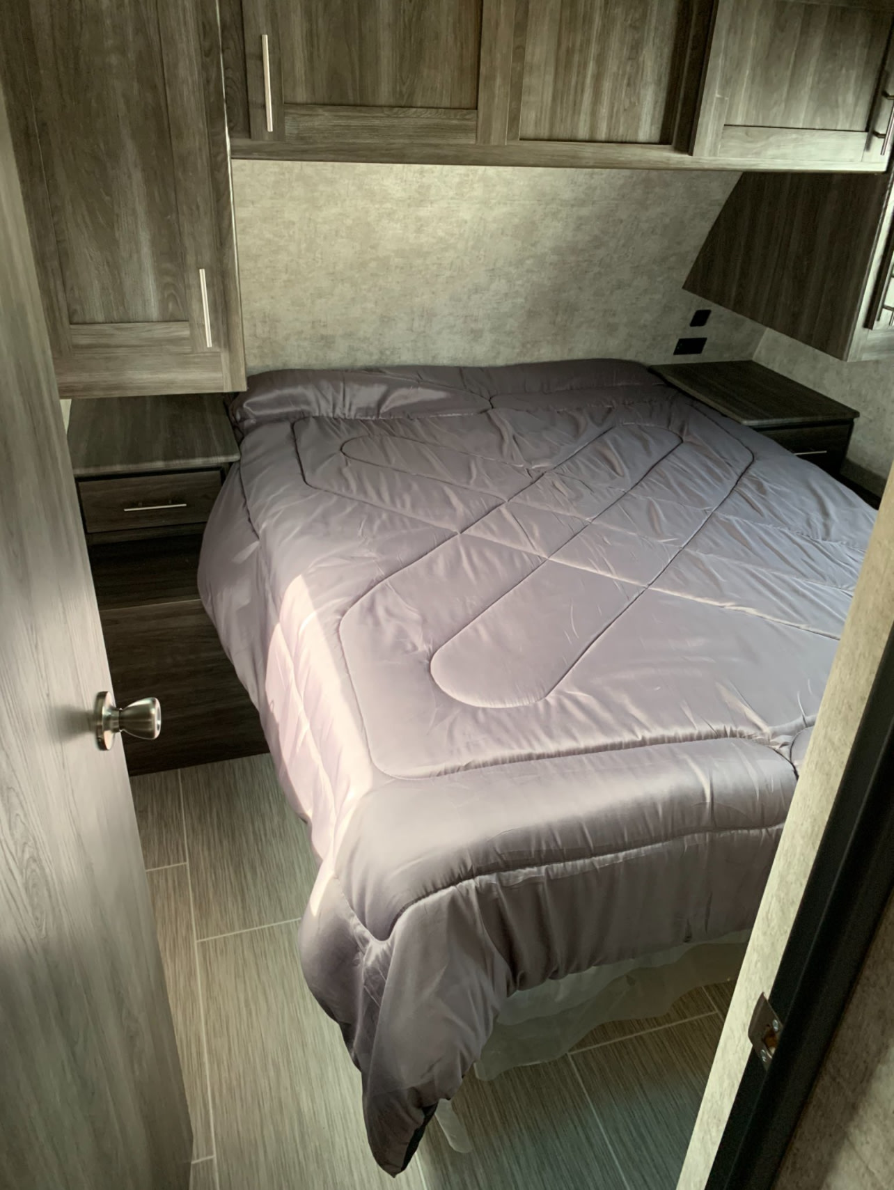 Experience compact comfort! This RV rental bedroom features a gray bed, dual nightstands, and overhead cabinets for storage.. Highland Ridge RV Mesa Ridge 2019