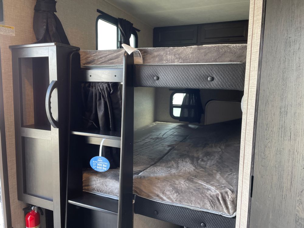 This inviting rv rental interior features comfortable bunk beds. A fire extinguisher and weight capacity details are visible.. Jayco Eagle HT 2023