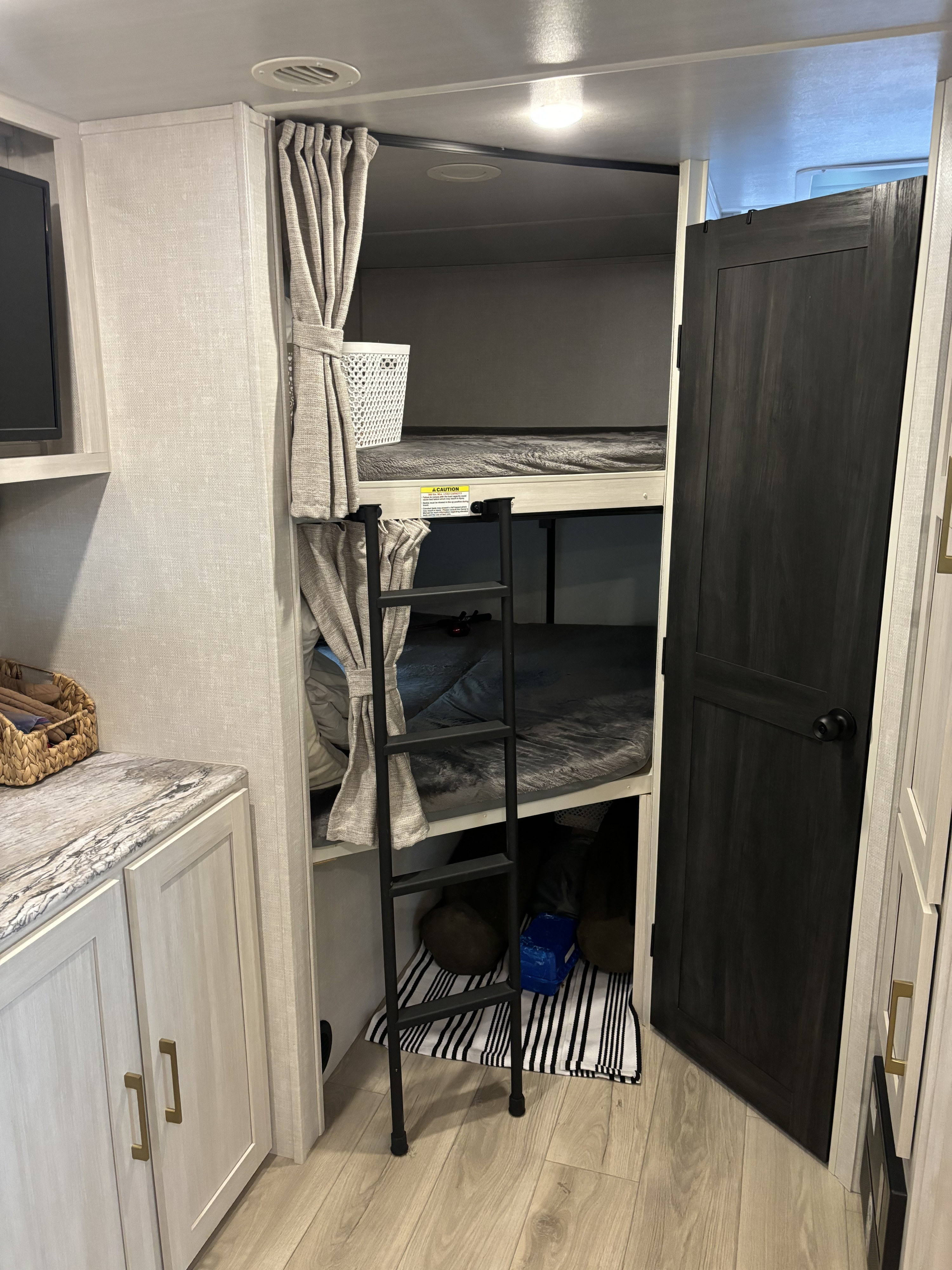 An RV rental interior reveals two stacked bunk beds with privacy curtains, a ladder, and compact living space.. Forest River Surveyor Legend 2024