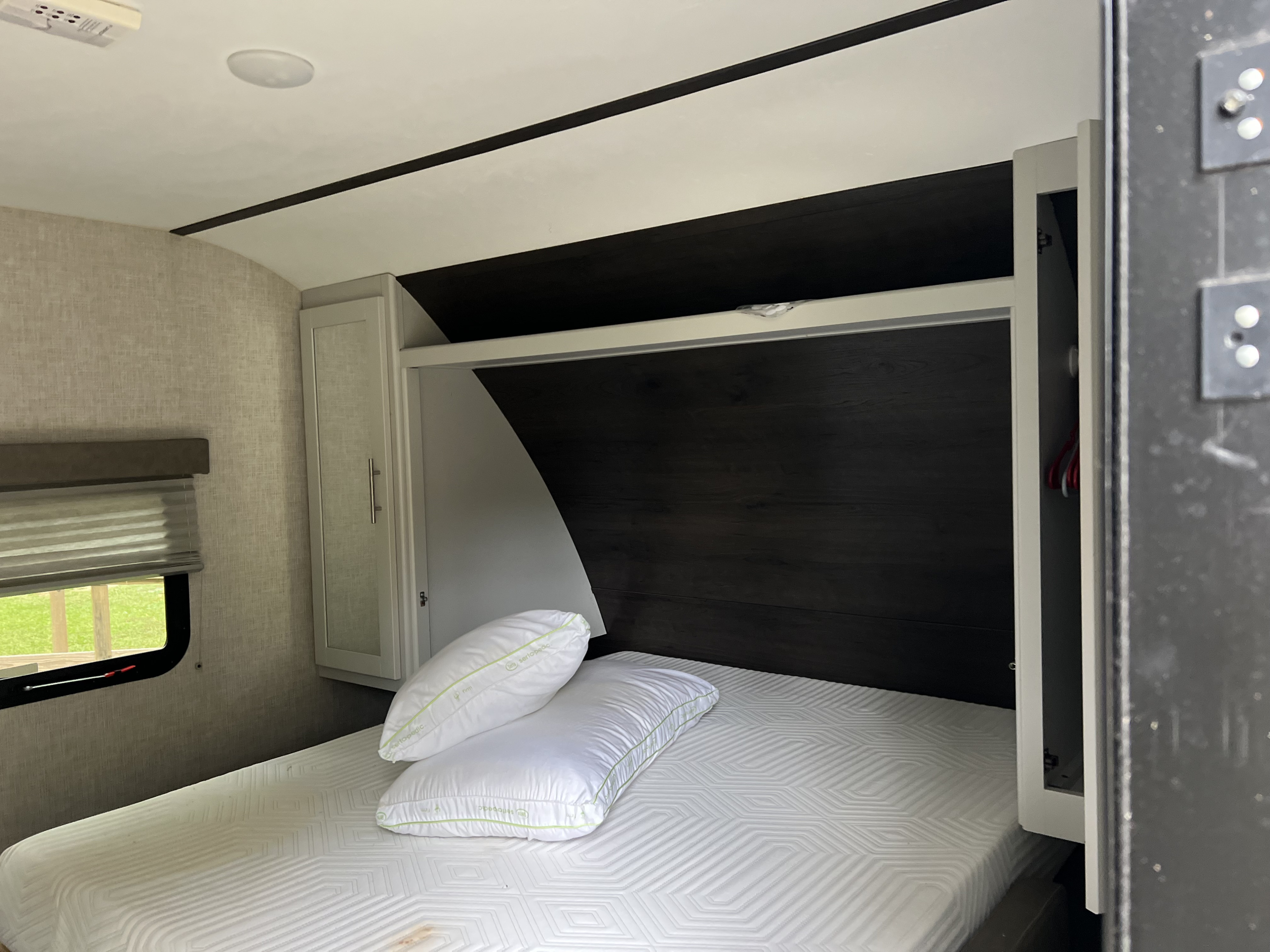Cozy RV rental bedroom featuring a comfortable bed with fresh pillows, dark wood headboard, and convenient storage cabinets.. Keystone RV Bullet Crossfire 2019