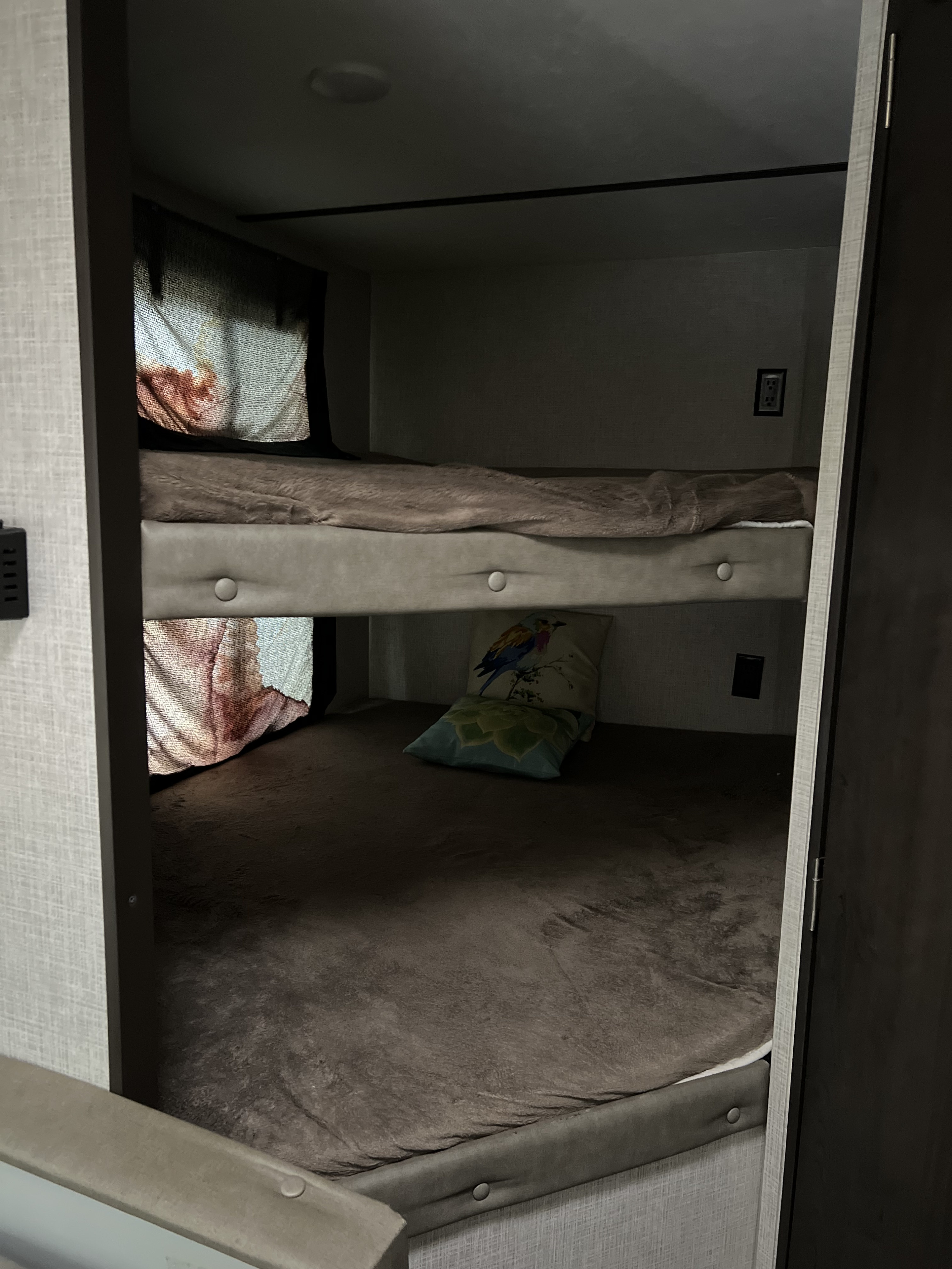 Cozy RV rental bunk beds: dimly lit sleeping area with two bunks, blankets, and decorative pillows inside a camper.. Keystone RV Bullet Crossfire 2019