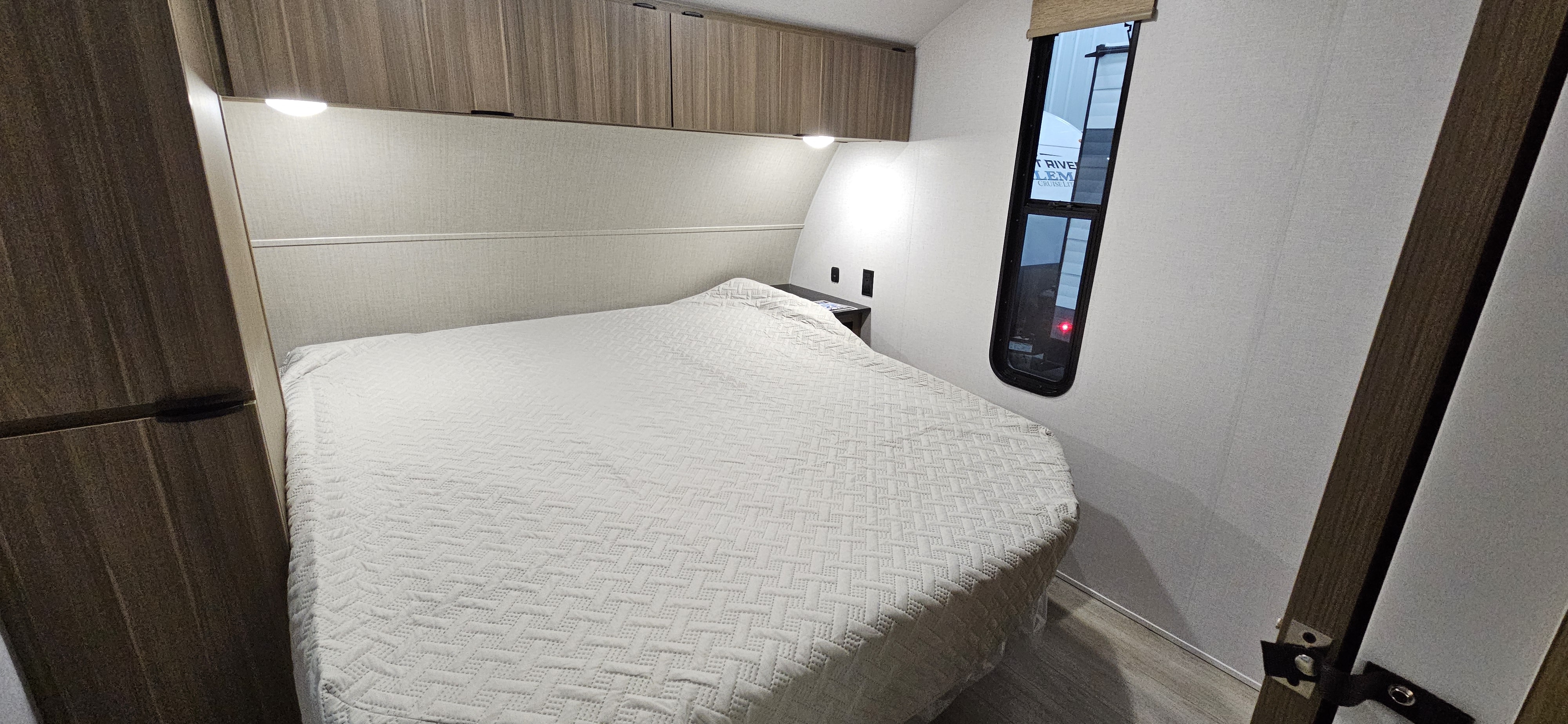 RV rental bedroom featuring a comfy bed with overhead storage, a small nightstand, and a side window.. Forest River-Salem Cruise Lite 26ICE 2025