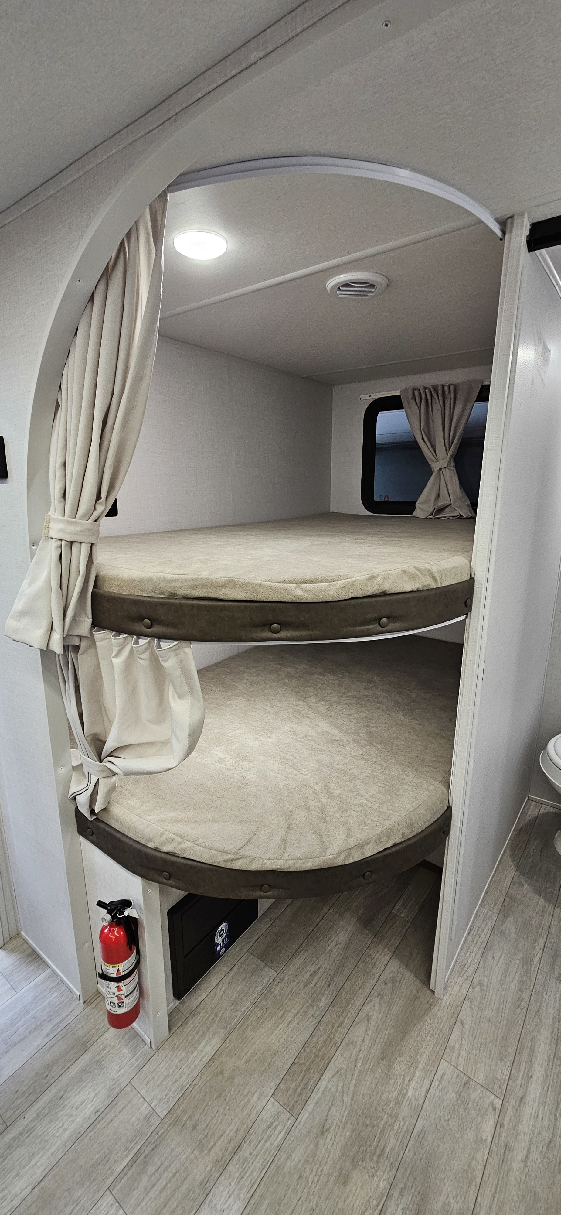 Cozy RV rental bunk beds with privacy curtains, ideal for family trips. Features a fire extinguisher and a window.. Forest River-Salem Cruise Lite 26ICE 2025