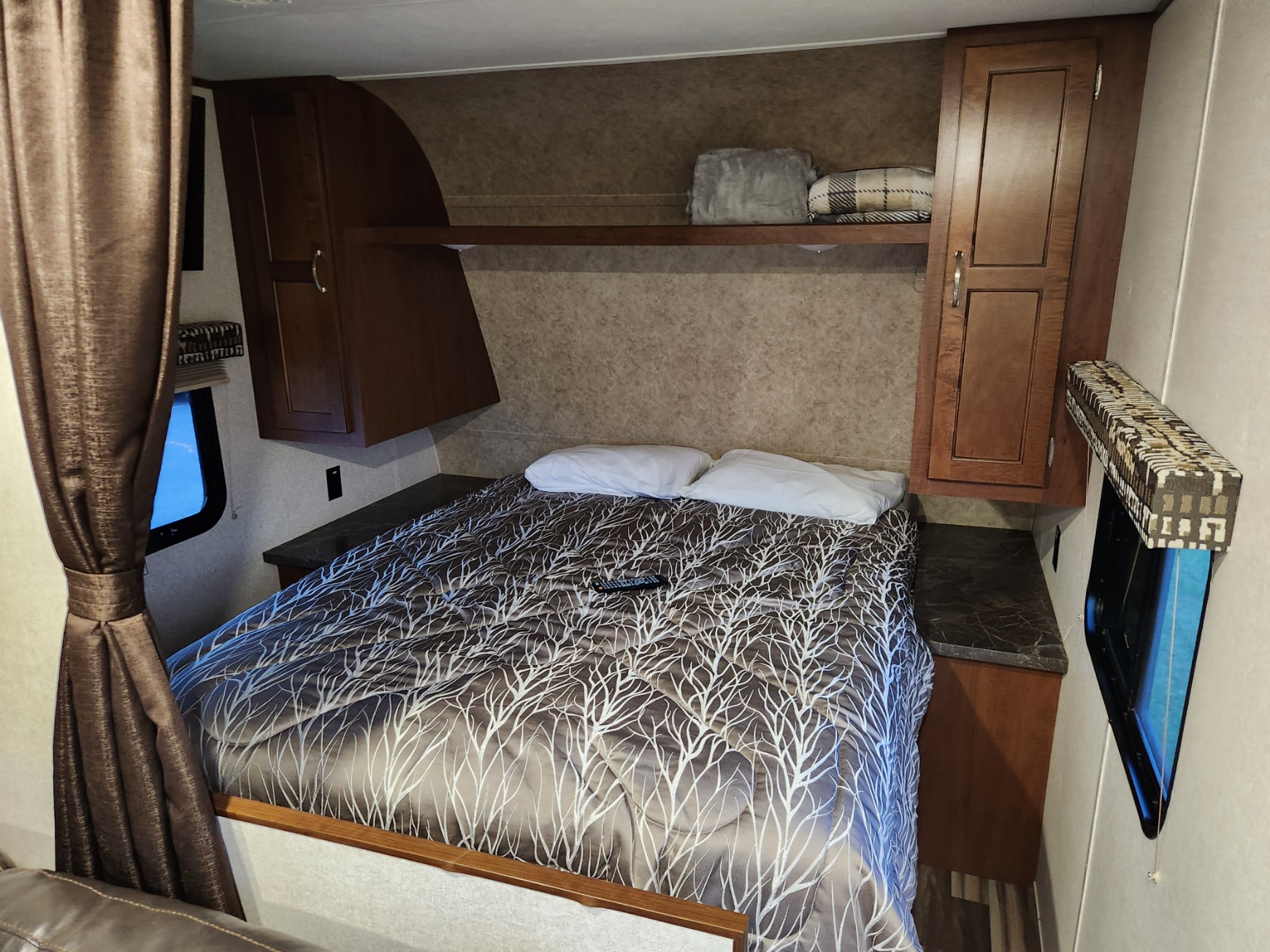 RV rental interior showing a compact bedroom with a patterned bed, two pillows, overhead storage, and side cabinets.. Jayco Jay Flight SLX 2017