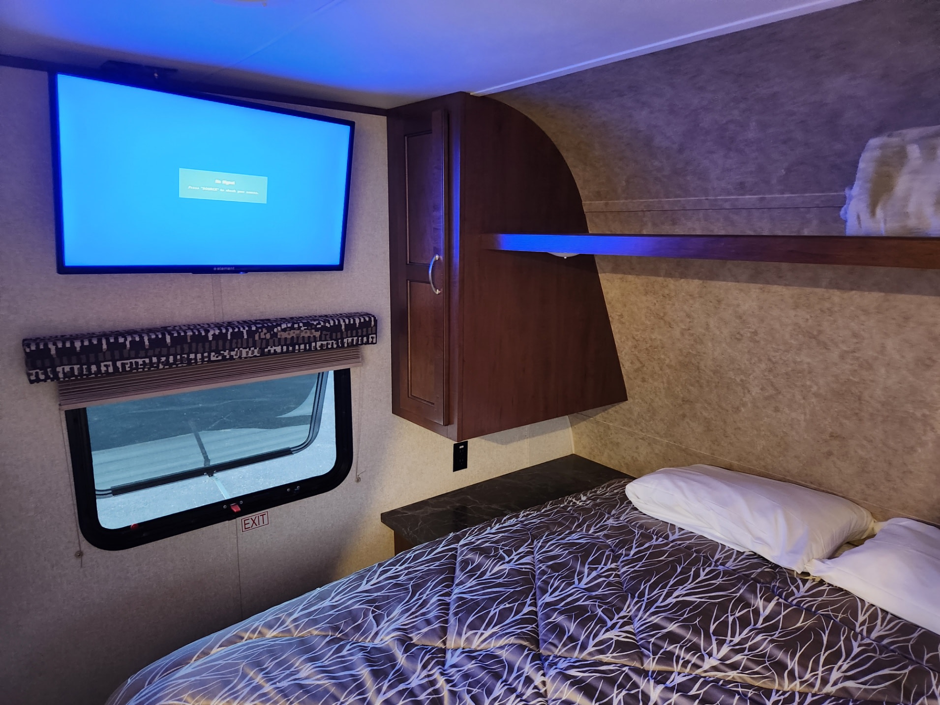 Inside an RV rental, a comfy bedroom features a TV, window, and cabinetry, all illuminated by blue ambient light.. Jayco Jay Flight SLX 2017