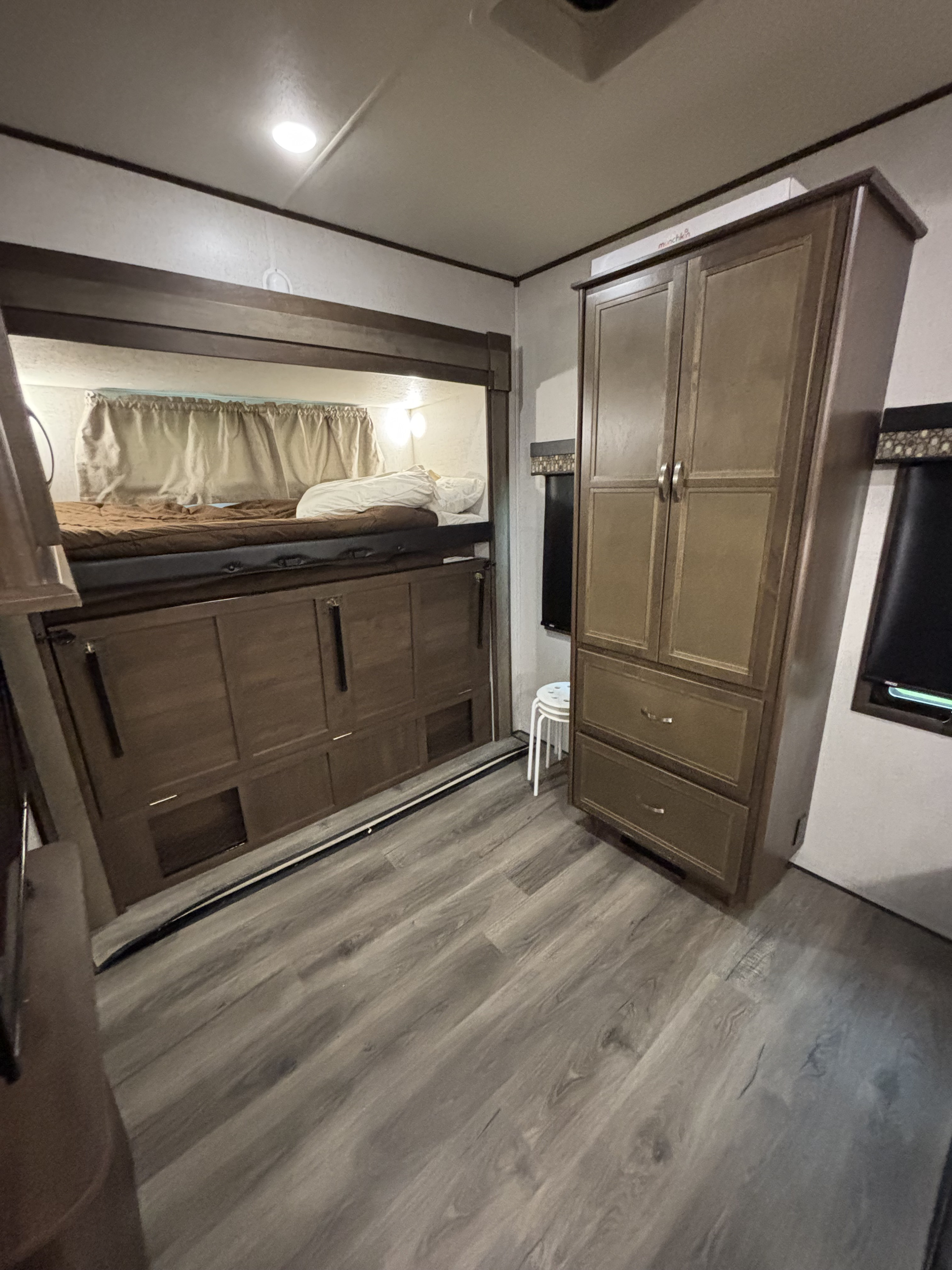 RV rental bunk bed area with brown bedding, storage below, and a tall cabinet/wardrobe nearby.. Highland Ridge RV Open Range 2020