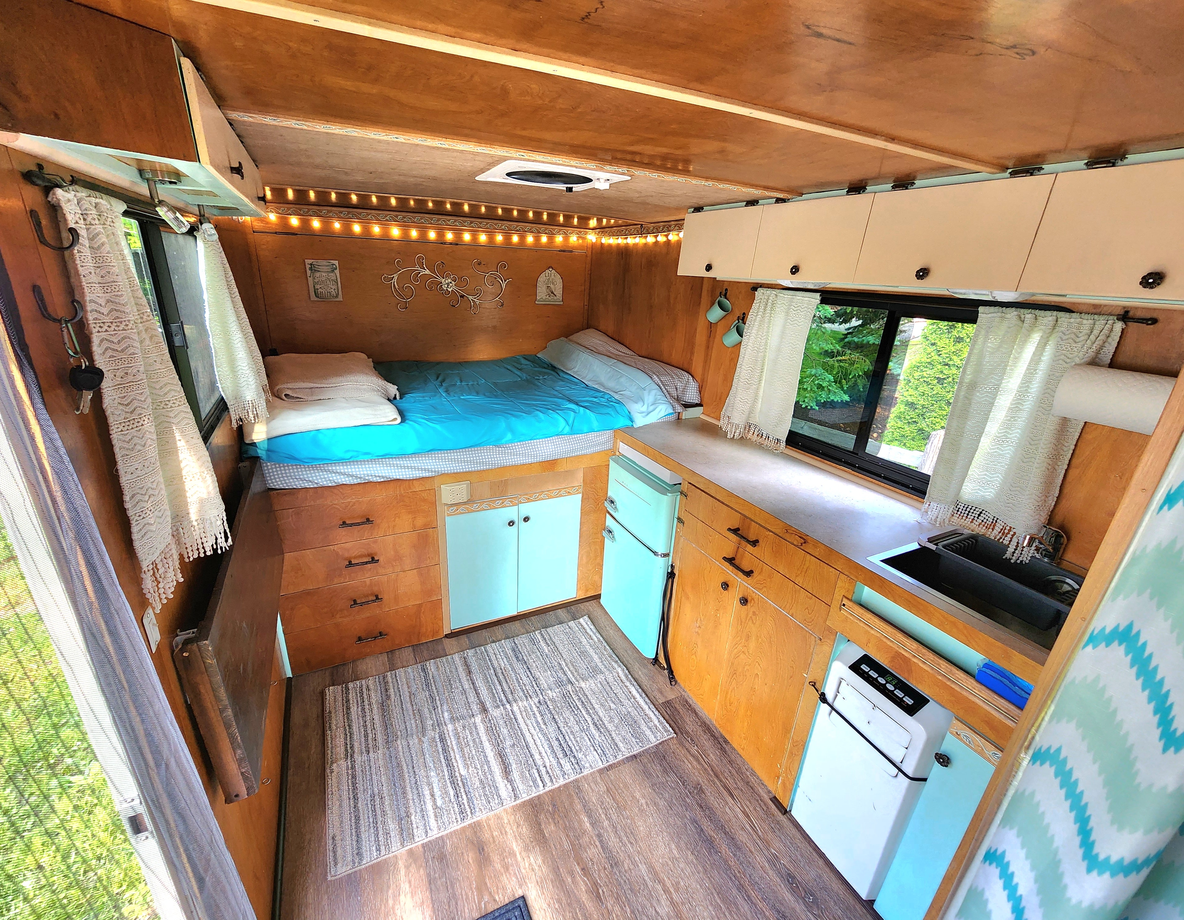 Inside a cozy RV rental: features a comfortable bed, compact kitchen with fridge & sink, and warm wood paneling.. Freedom 7x14TA2 2018