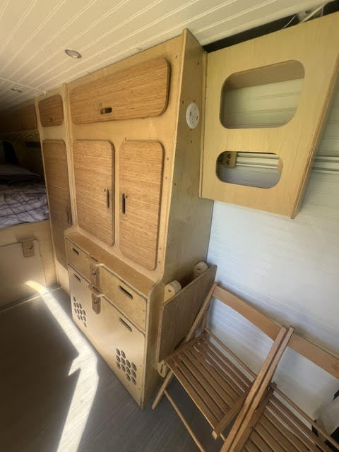 RV rental interior featuring clever wooden cabinetry, ample storage, and a stowed folding chair for compact living.. Mercedez Sprinter 2016