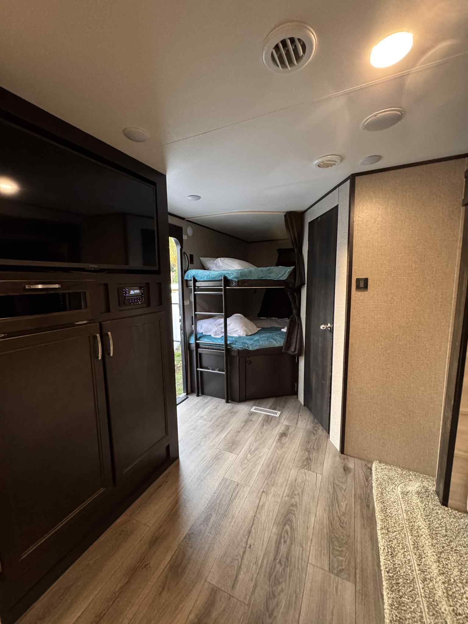 Inside a modern RV rental: dark wood entertainment unit, comfy bunk beds, and light laminate flooring.. Jayco Jay Flight 2021