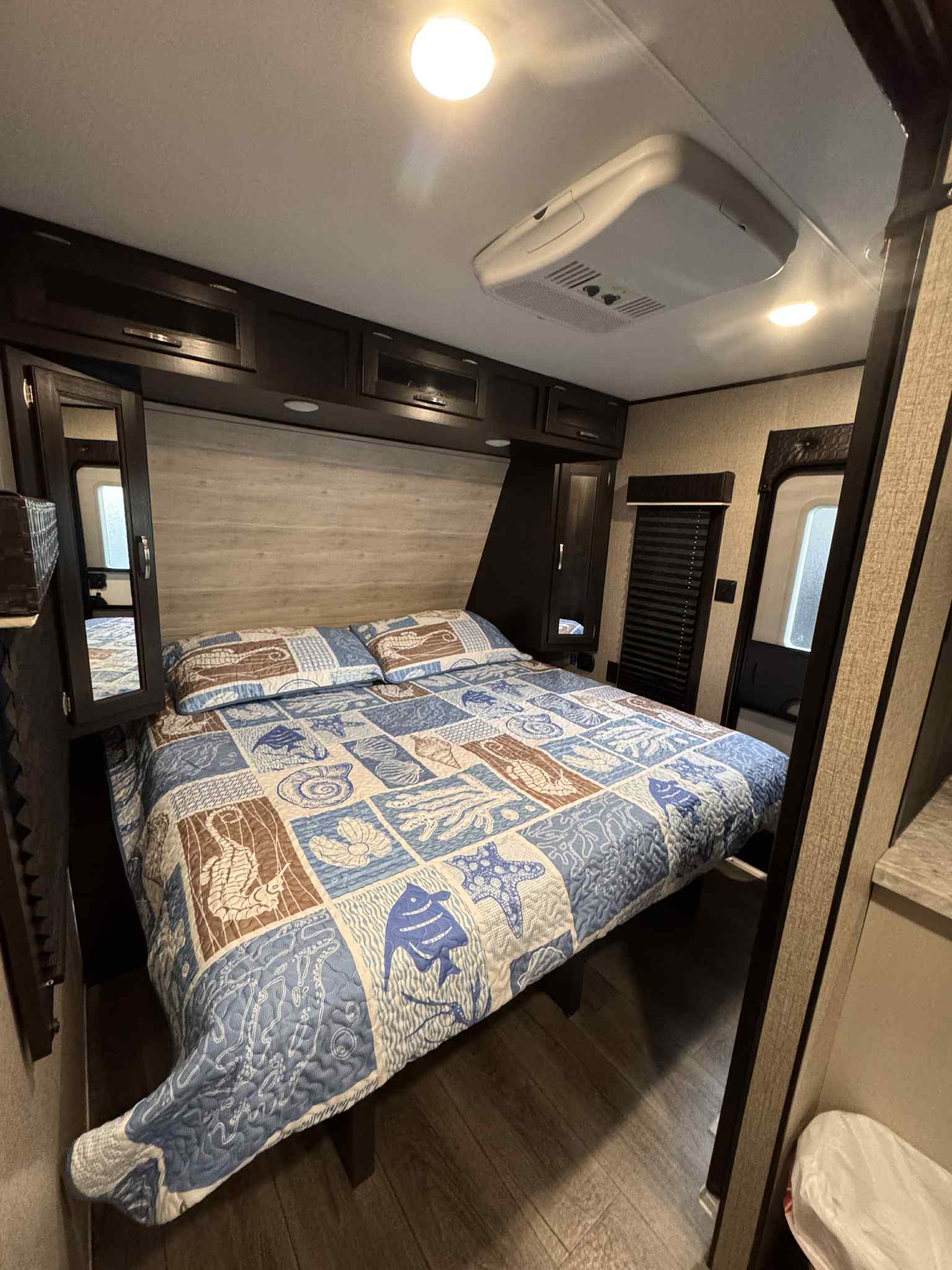 Inside this RV rental, a well-appointed bedroom features a large bed with a patterned quilt, overhead storage, and an AC unit.. Jayco Jay Flight 2021