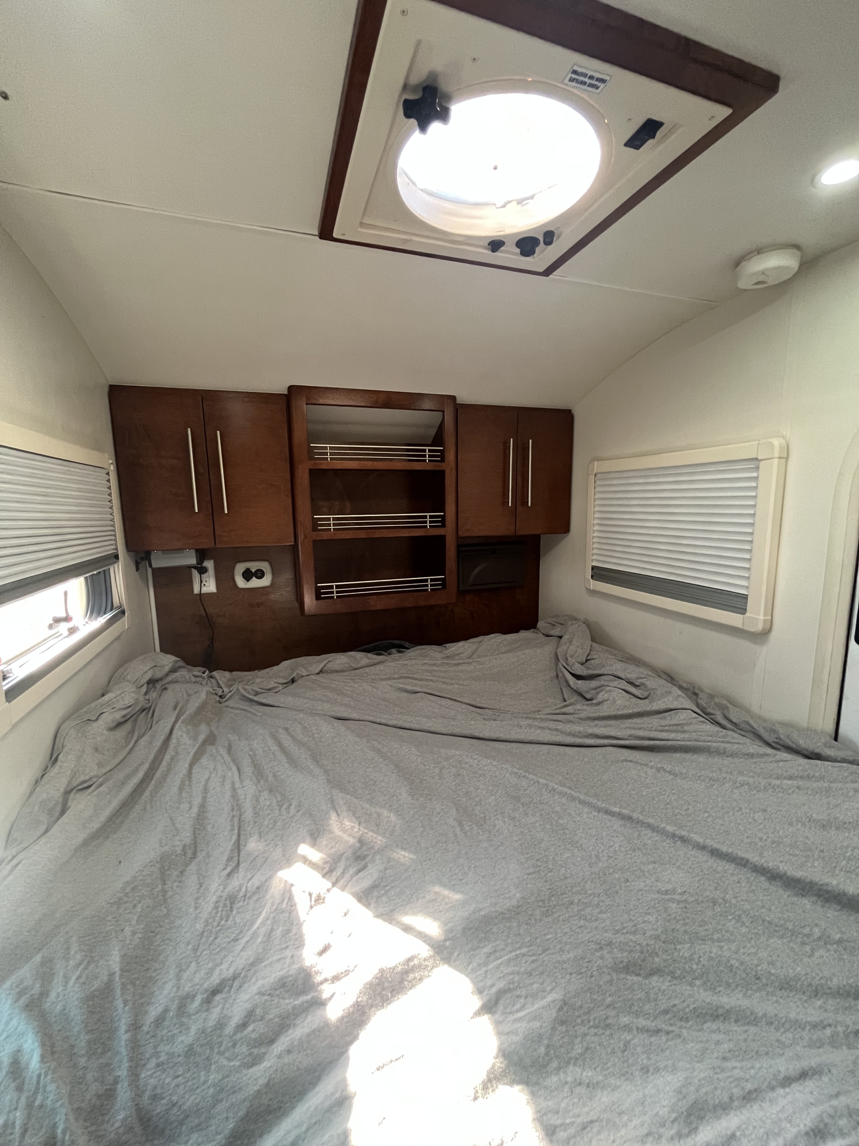 RV rental bedroom with a large bed, wooden overhead cabinets, windows with blinds, and a bright roof vent.. T@G T@G Teardrop Trailer 2015