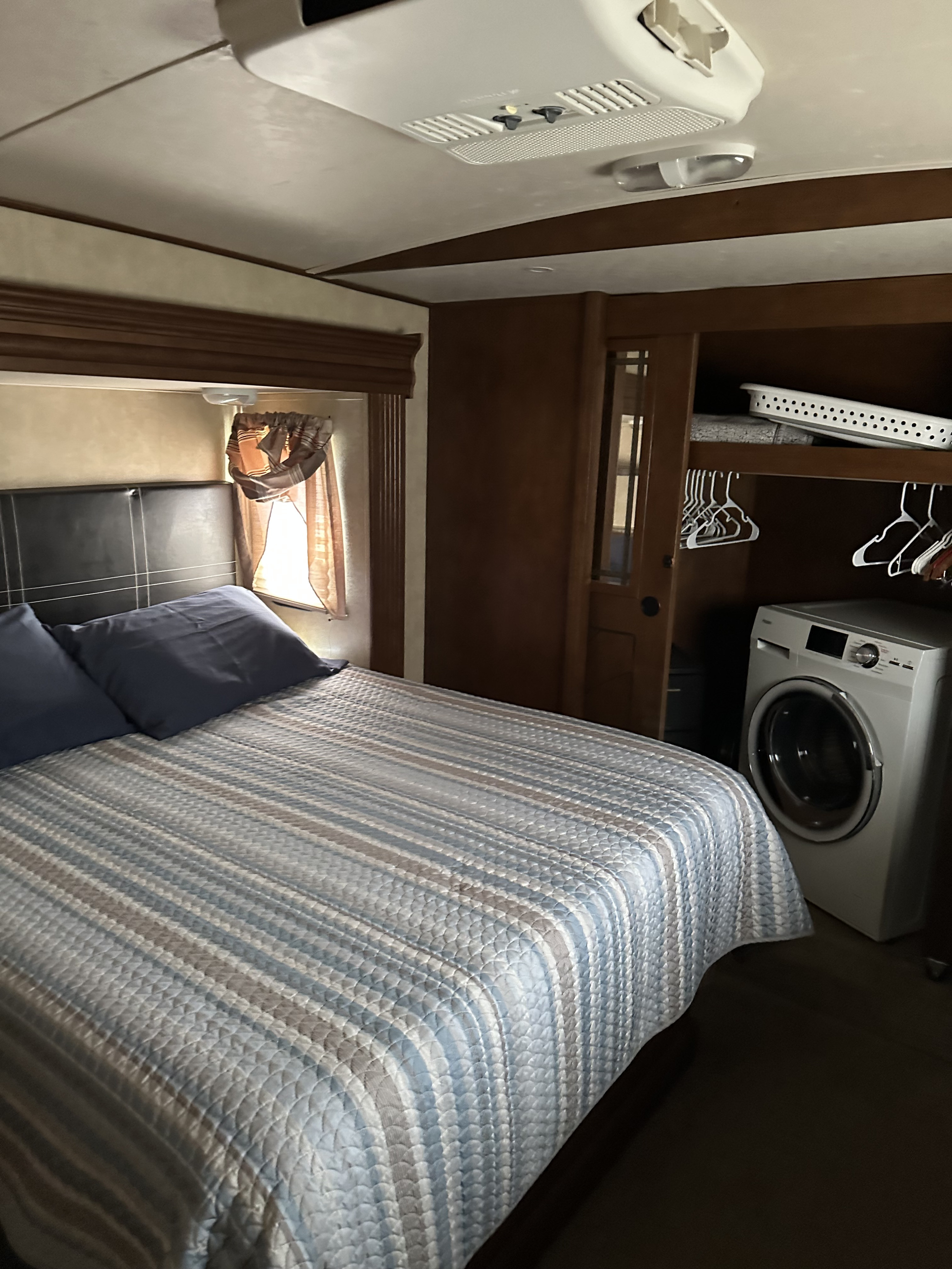 RV rental bedroom with patterned bed, window, and an accessible washer/dryer unit inside a closet.. Forest River Salem Hemisphere Lite 2015