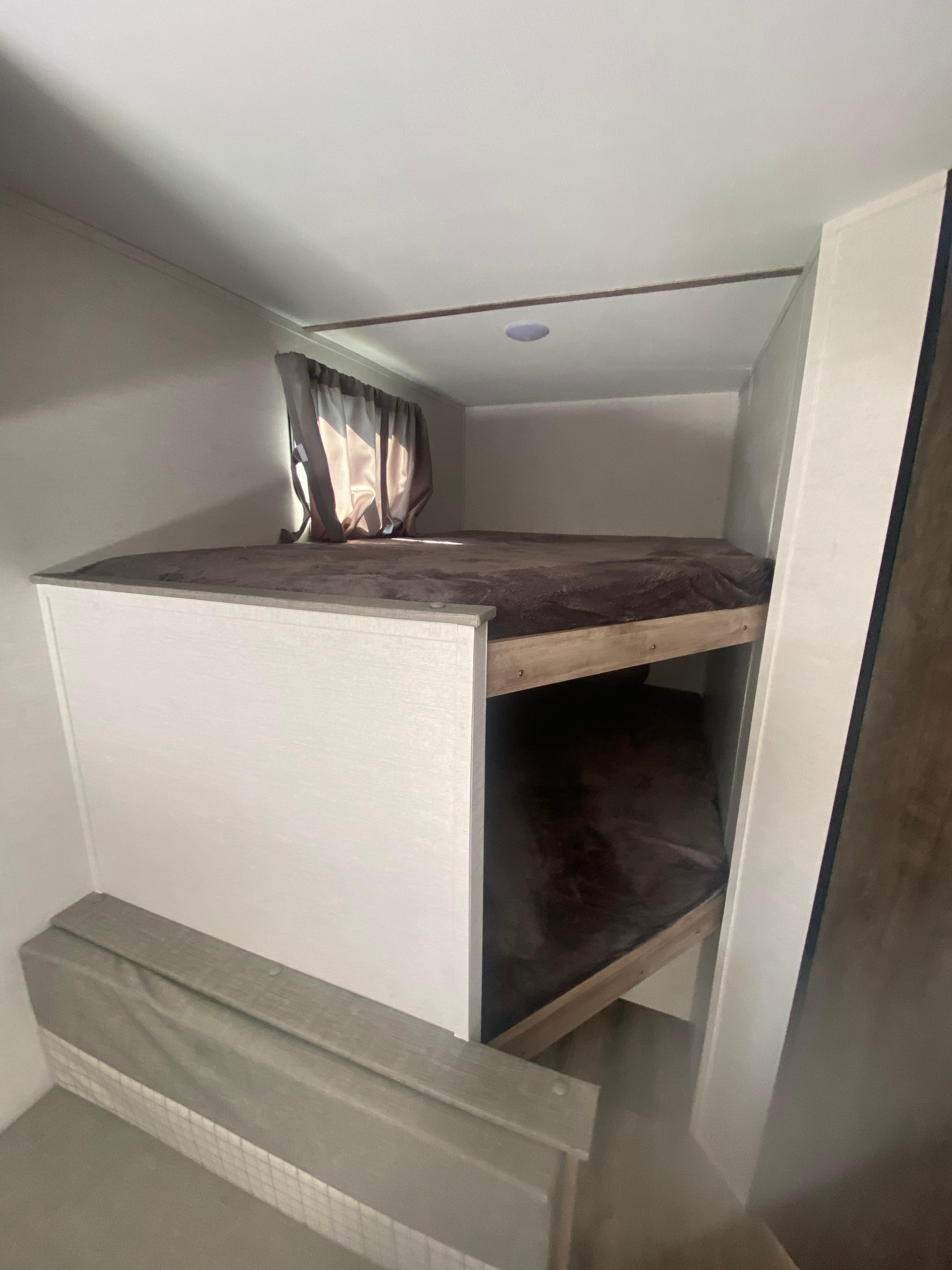 Cozy bunk beds with brown bedding and window with curtains inside an RV rental, ideal for family travel.. Gulf Stream Grand River 2024