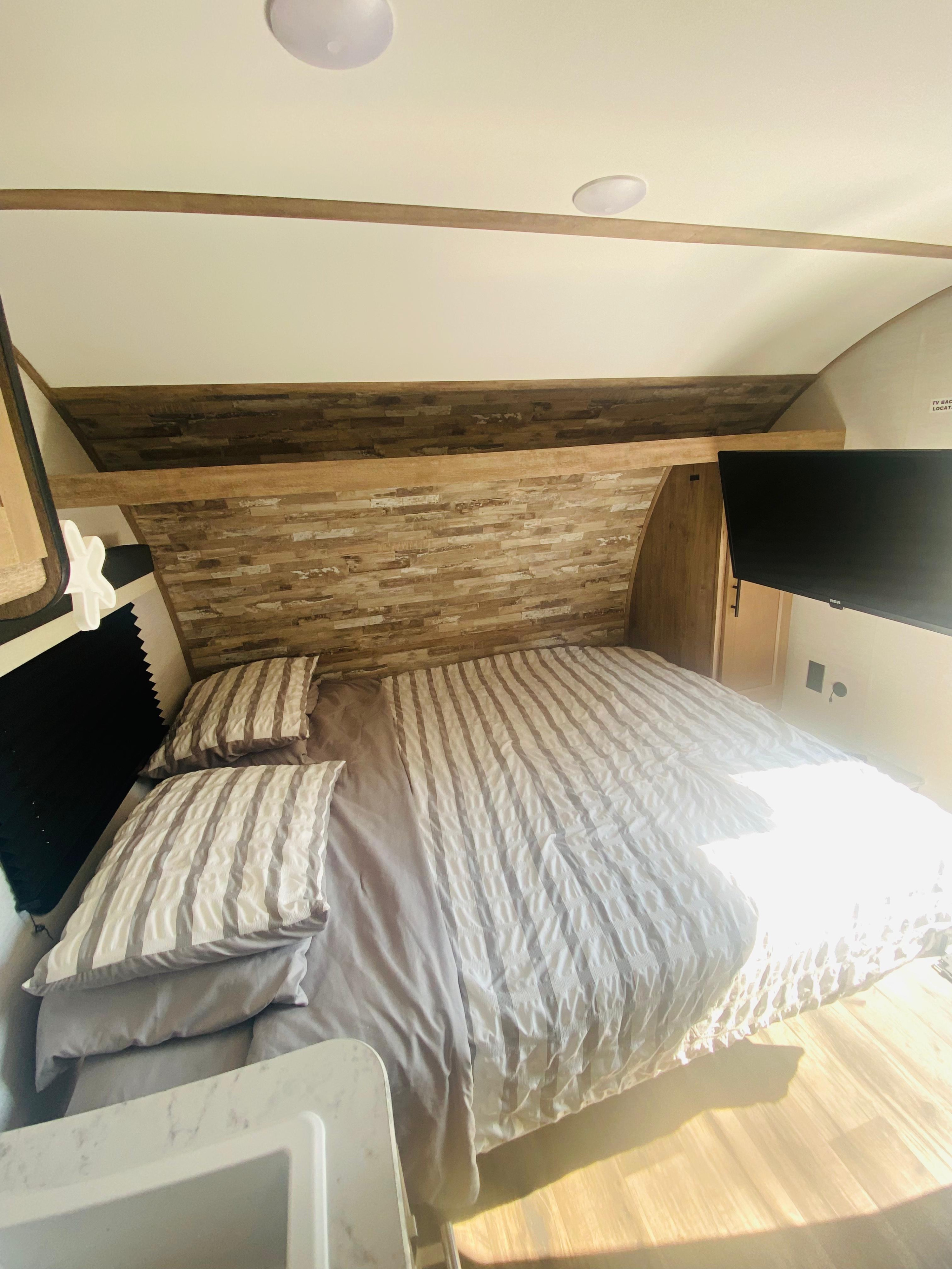 RV rental bedroom with a comfy bed, gray striped bedding, wood-paneled walls, and a mounted TV on the right.. Gulf Stream Grand River 2024