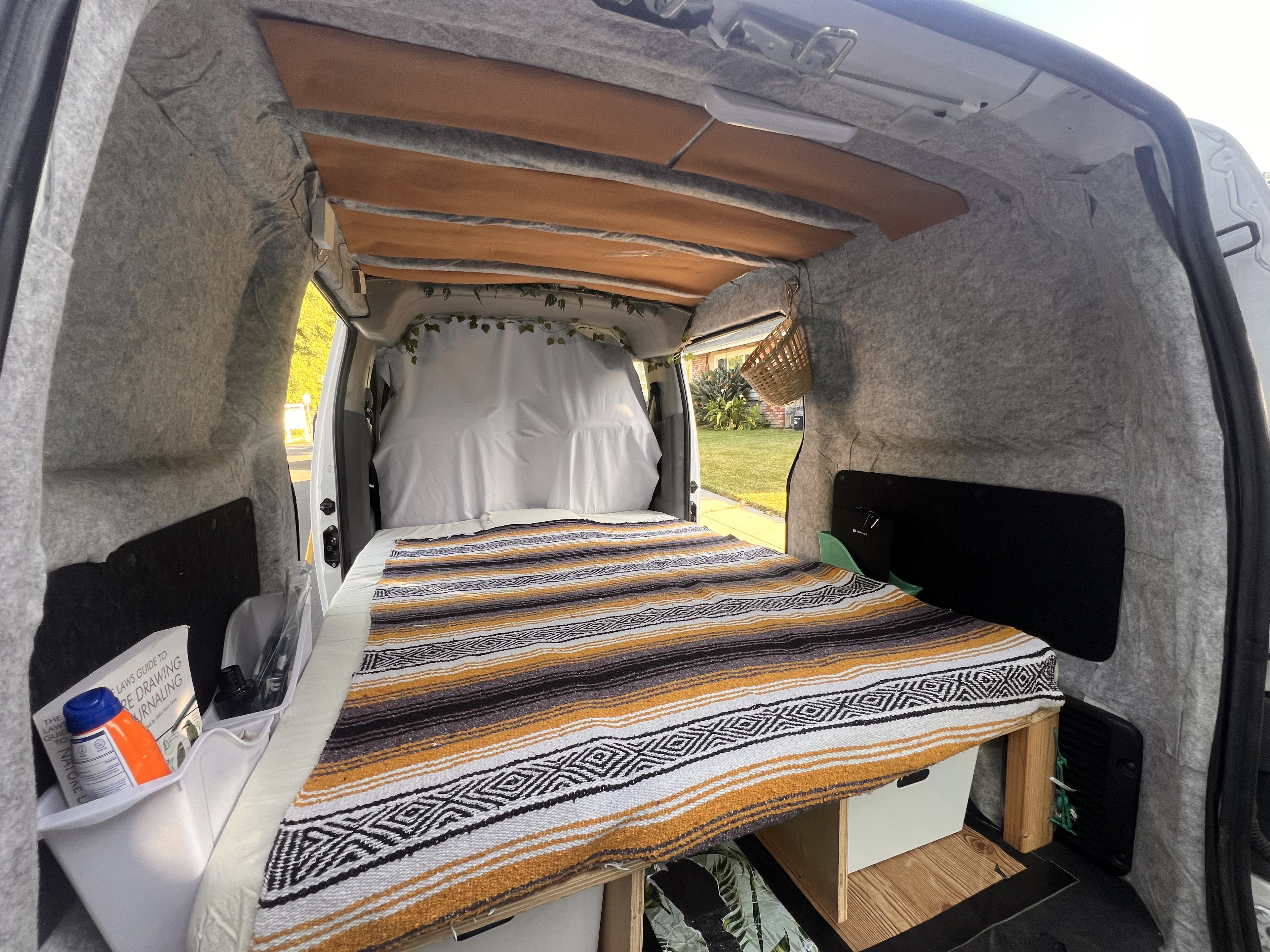 Cozy camper van RV rental interior: A built-in bed with striped blanket, fabric-lined walls, and clever storage solutions.. Nissan NV200 Compact Cargo 2019
