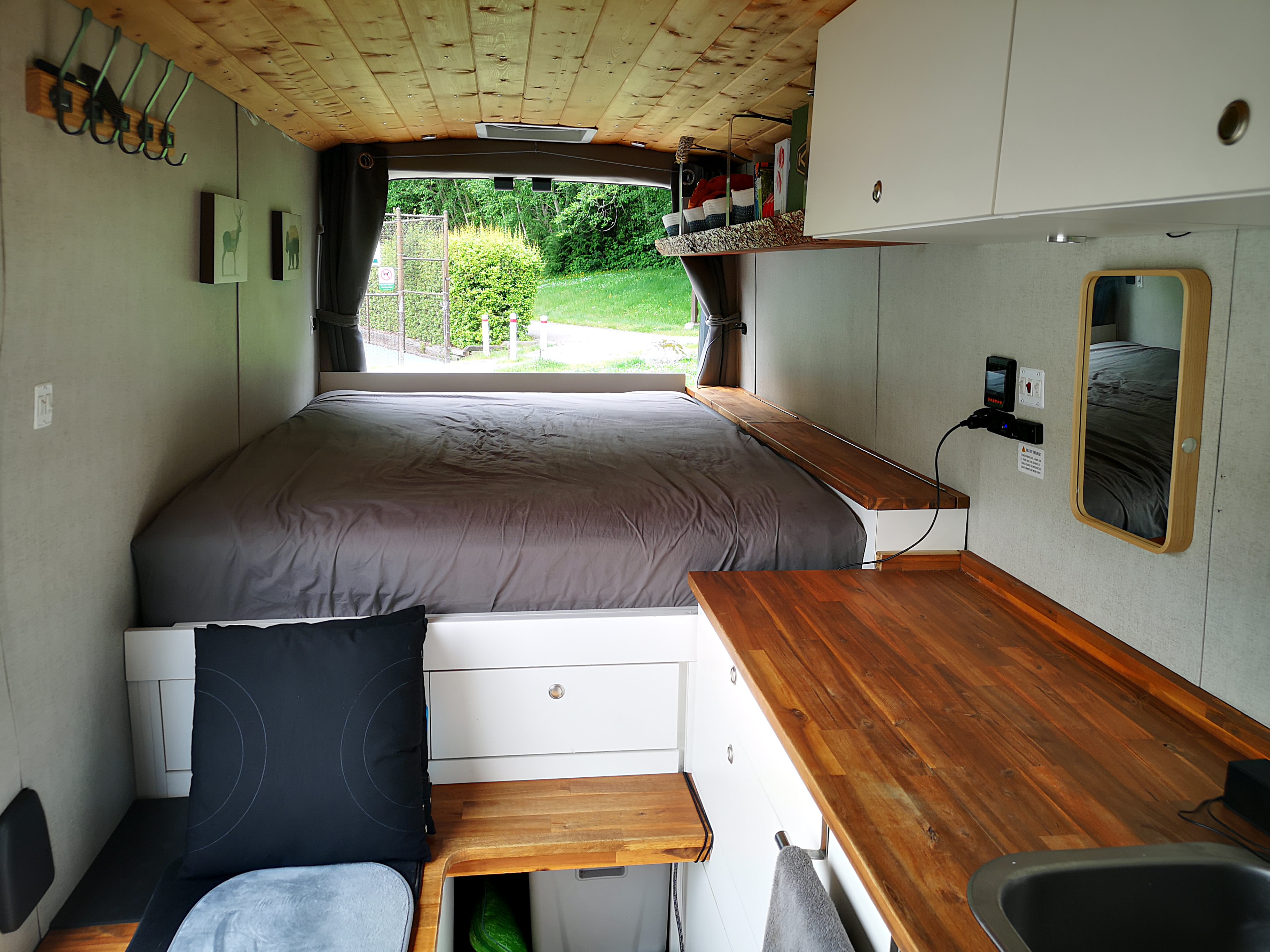 Step inside this cozy RV rental featuring a comfortable bed, wooden ceiling, and functional kitchen with a sink.. Ford Transit 2022