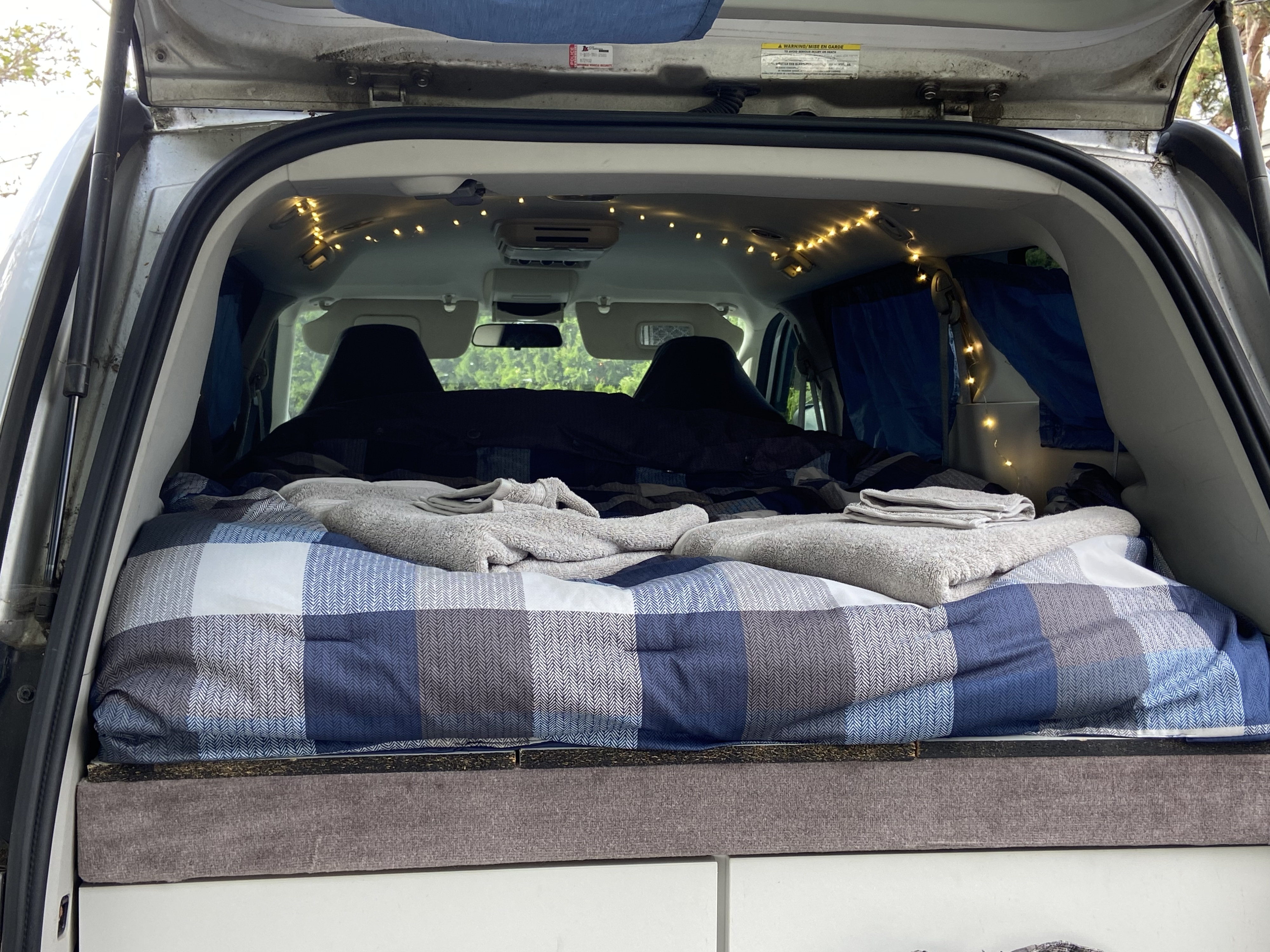 Cozy rv rental camper van interior with plaid bedding, string lights, and folded towels on a comfortable bed setup.. Dodge Grand Caravan 2008
