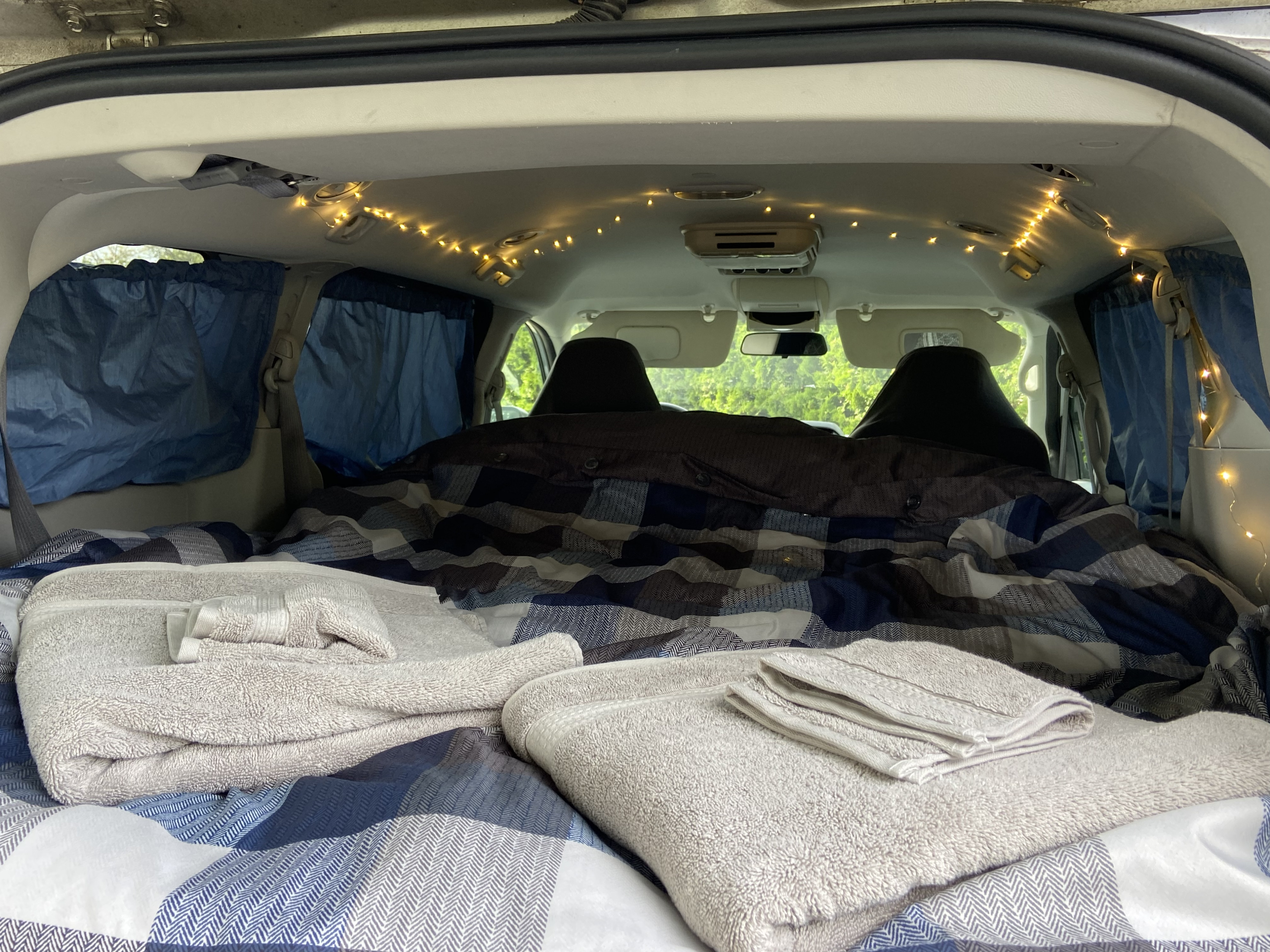 Inside this **rv rental**: a cozy bed with patterned bedding, soft towels, and ambient string lights for comfortable camping.. Dodge Grand Caravan 2008
