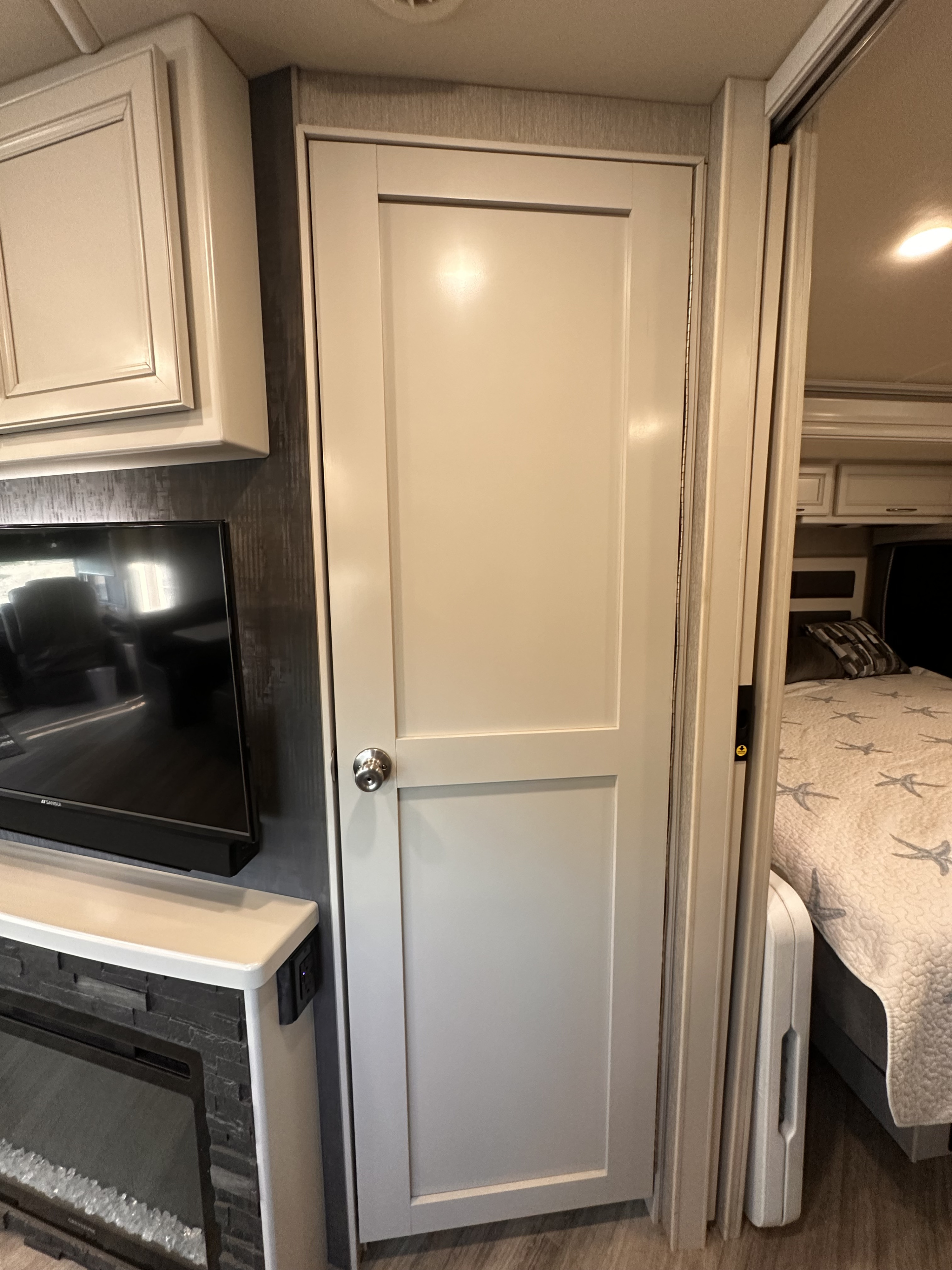 RV rental interior showing a white door dividing living area with TV & fireplace from the bedroom with a starfish-quilt bed.. Holiday Rambler Vacationer 2022