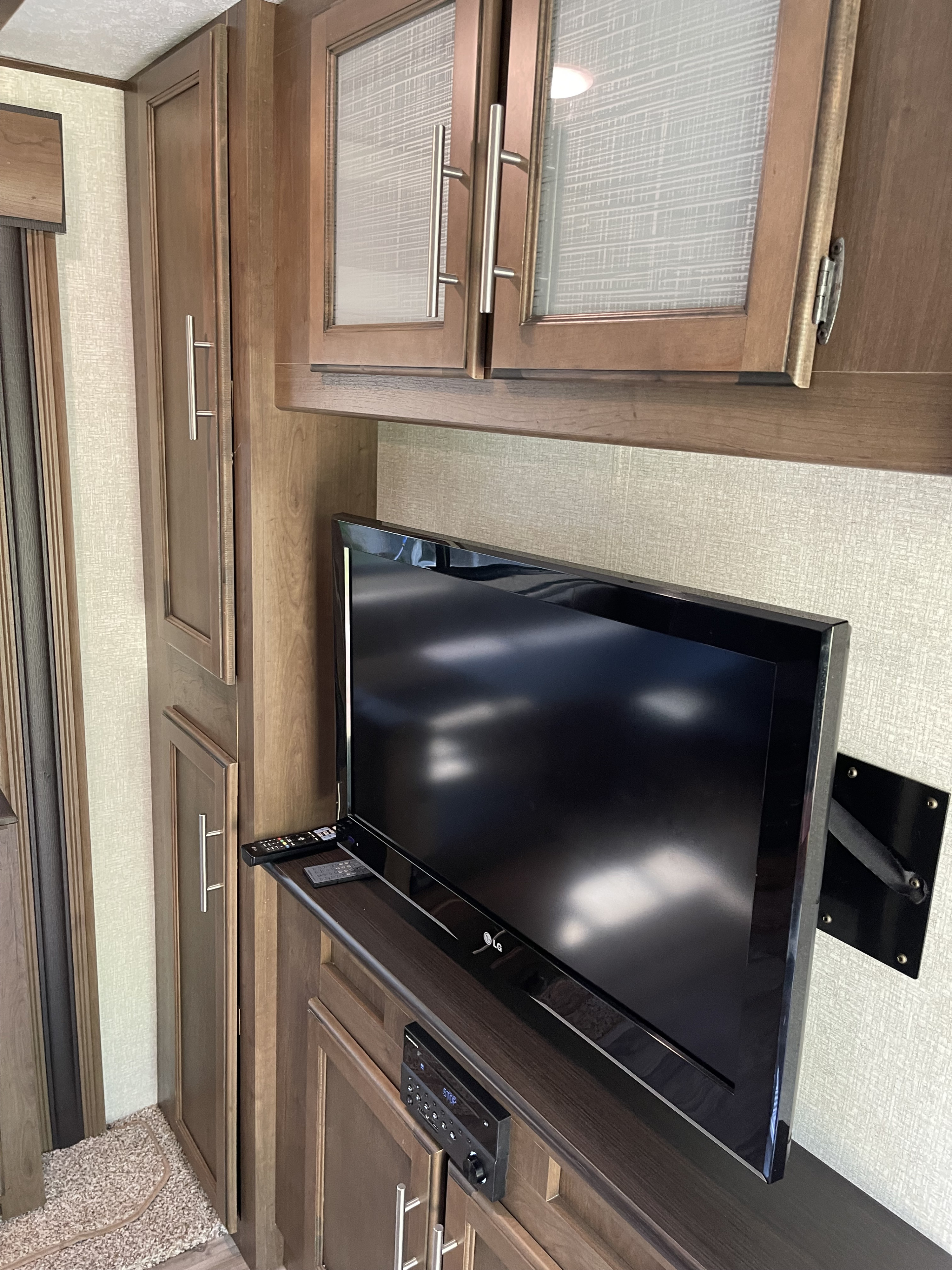 RV rental interior showcasing a mounted LG TV, integrated media player, and practical wooden cabinets for storage.. Keystone RV Cougar 2018