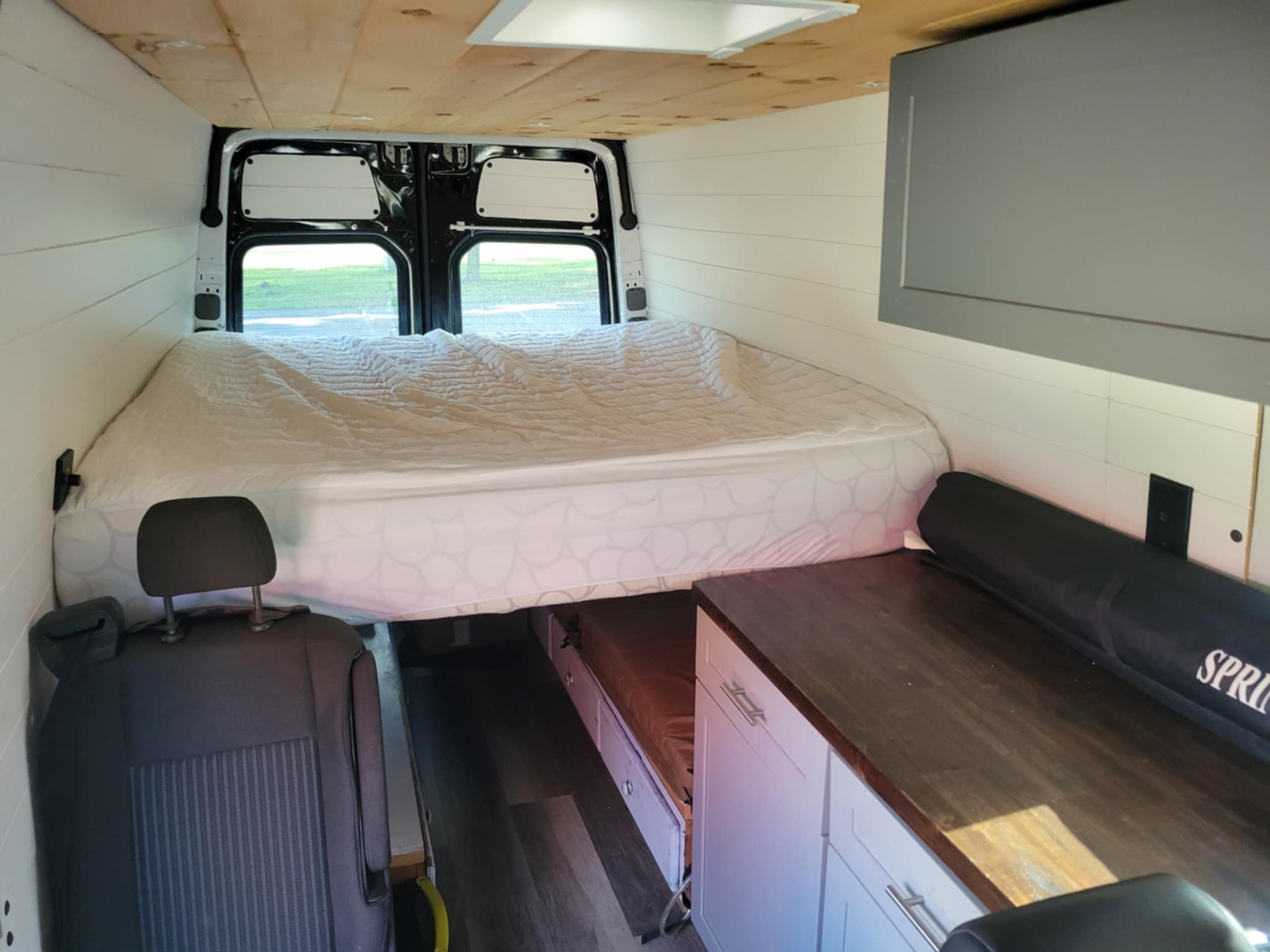 Inside a modern camper van conversion, ideal for RV rental. Features a comfy bed, efficient storage, and counter space.. Freightliner Sprinter 2011