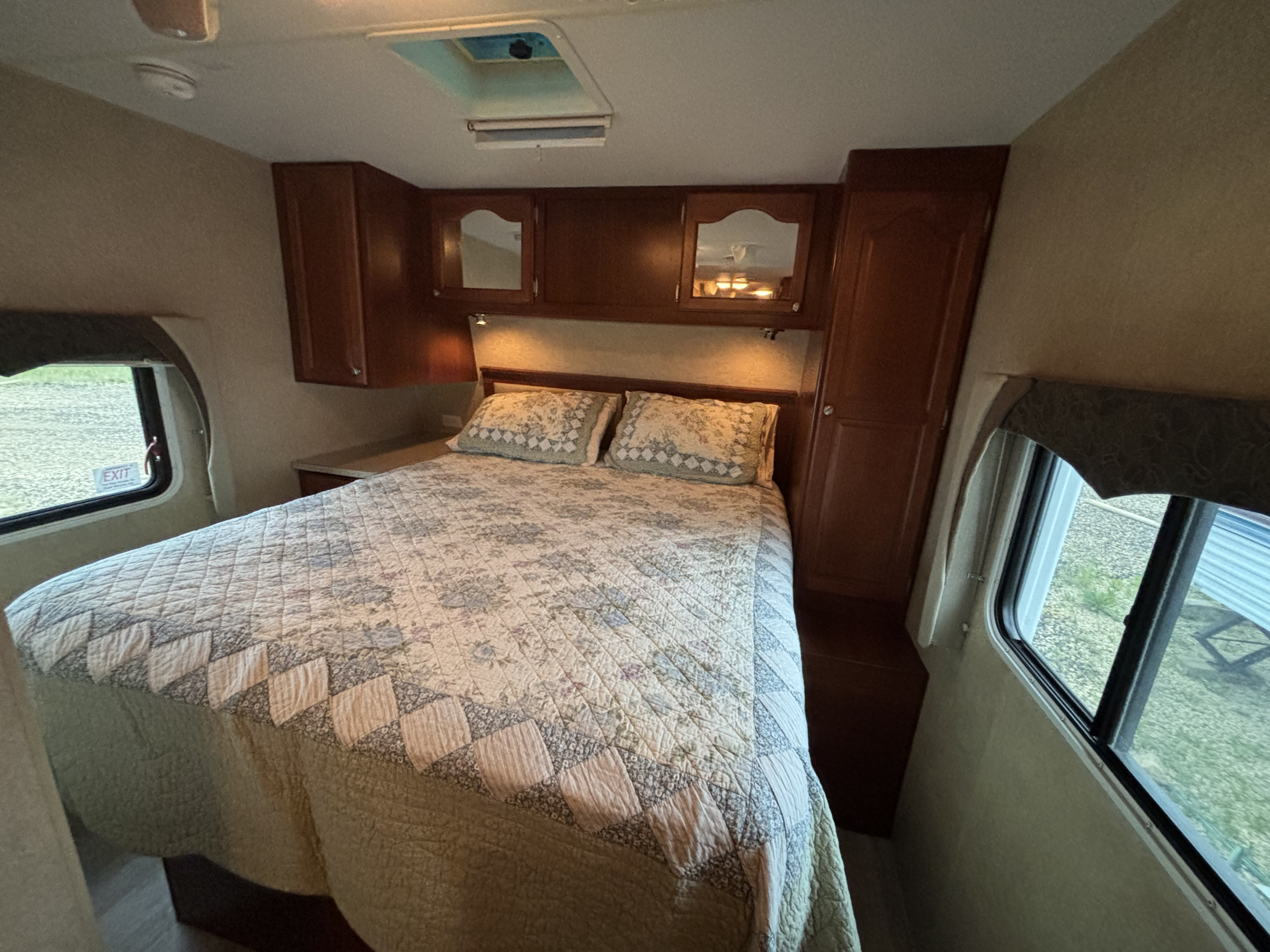 Inside this RV rental, find a cozy bedroom with a patterned bed, wood cabinets, ceiling vent, and emergency exit window.. Fleetwood 230RKS 2009