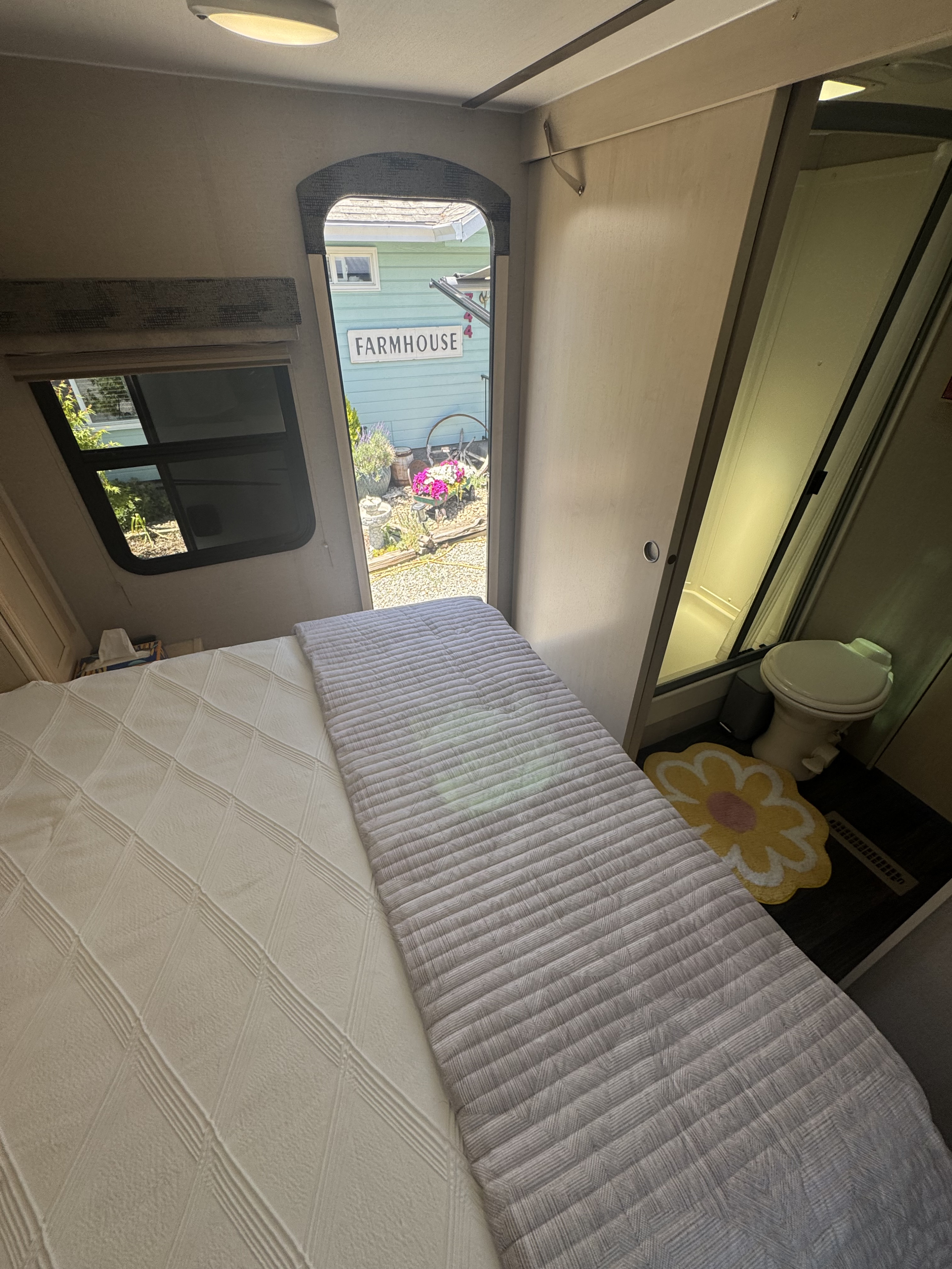 Inside an RV rental: a comfortable bed, view of a "Farmhouse" garden, and a small toilet/shower area.. Minnie Minnie Trailer 2019