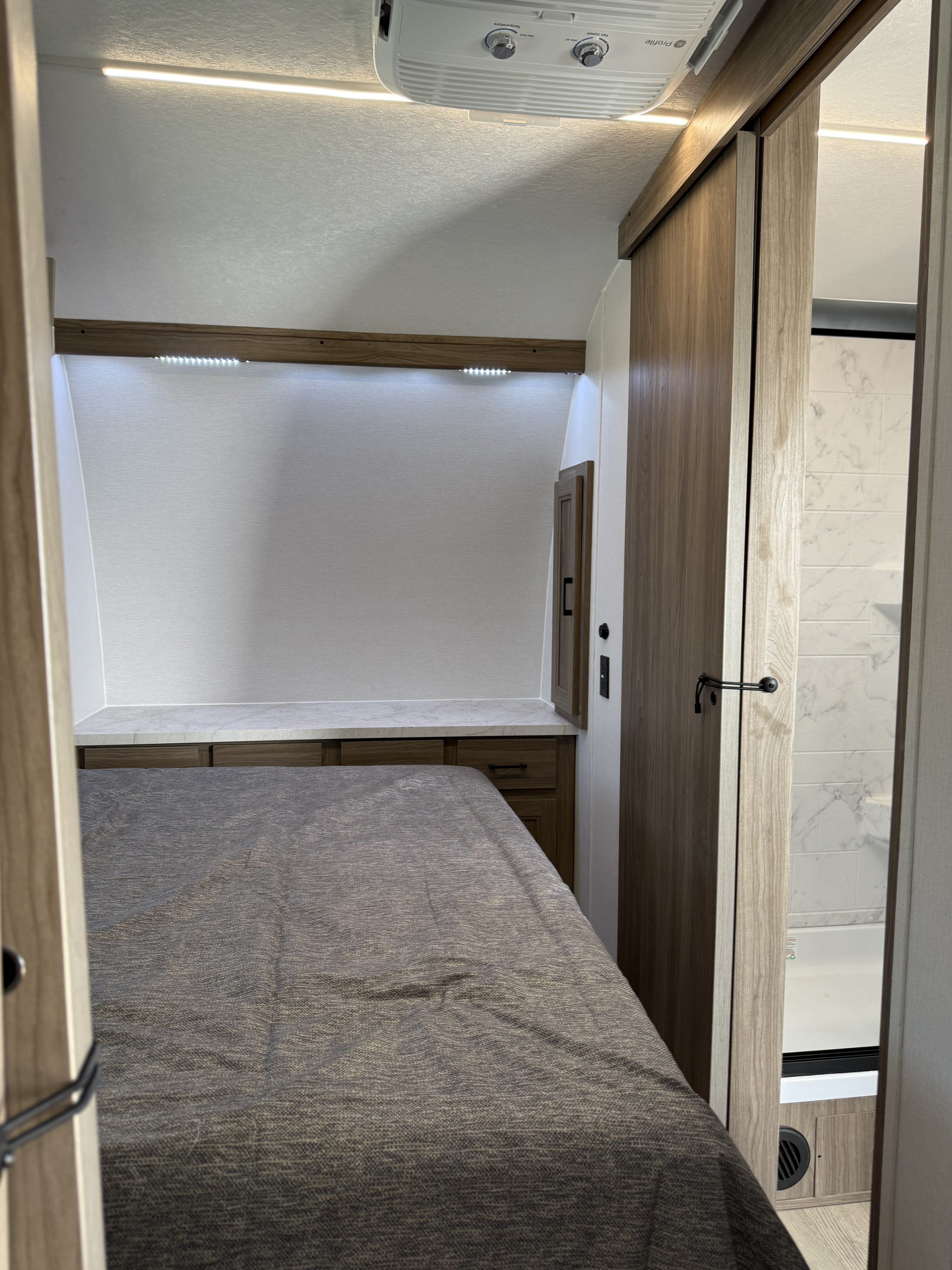 Cozy RV rental bedroom featuring a full bed, built-in storage, bright lighting, and an adjacent modern bathroom.. Coachmen Adrenaline 2025