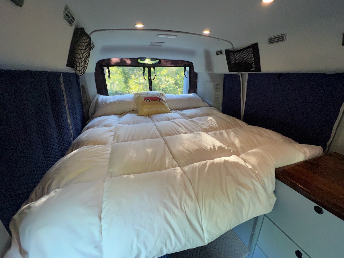 Cozy RV rental bedroom with large bed, pillows, and windows. Perfect for summer travel.. Ford Van 2019