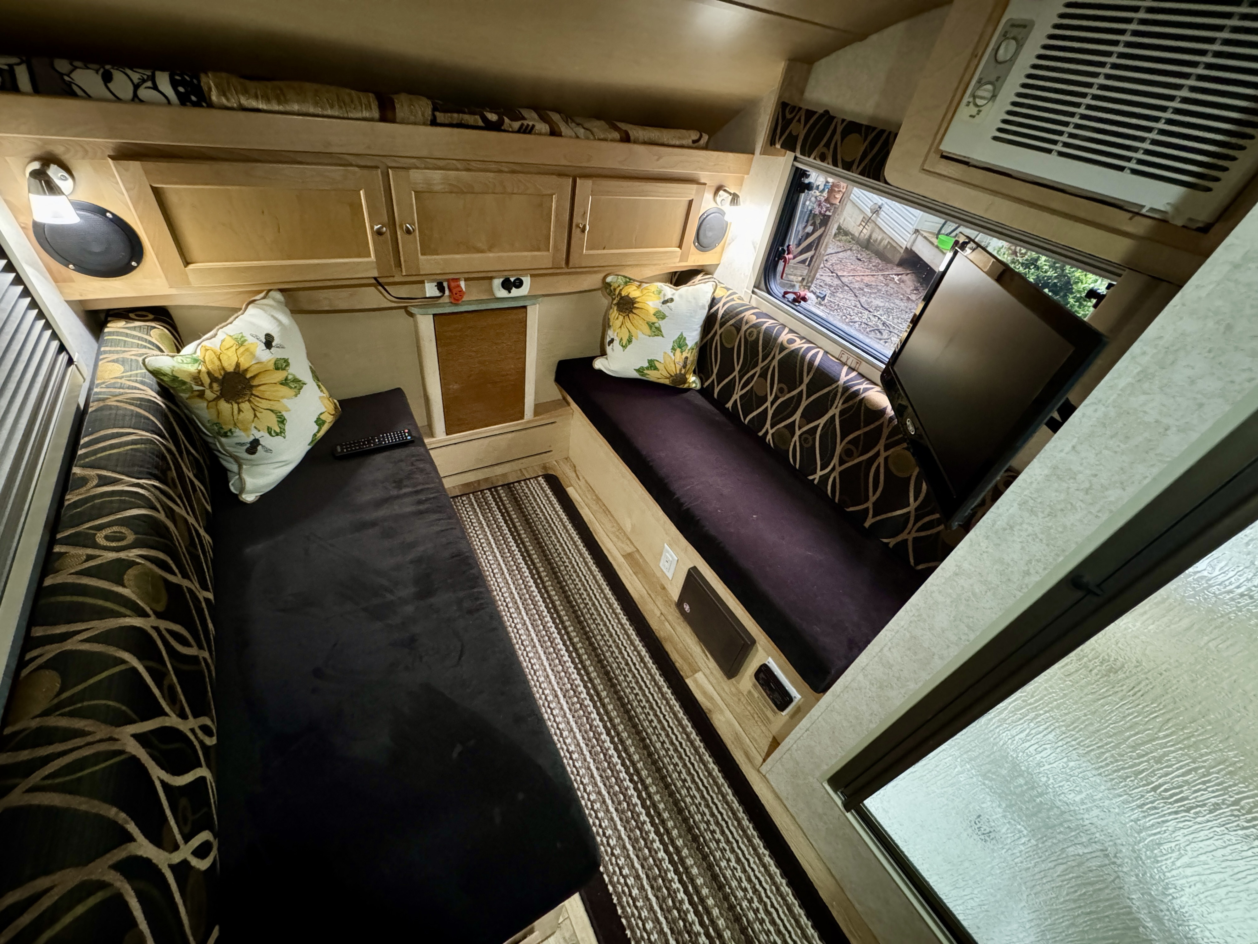 Inviting RV rental interior showcasing comfortable benches, sunflower pillows, overhead storage, AC, and a window.. Little Guy T@B CS-S 2015