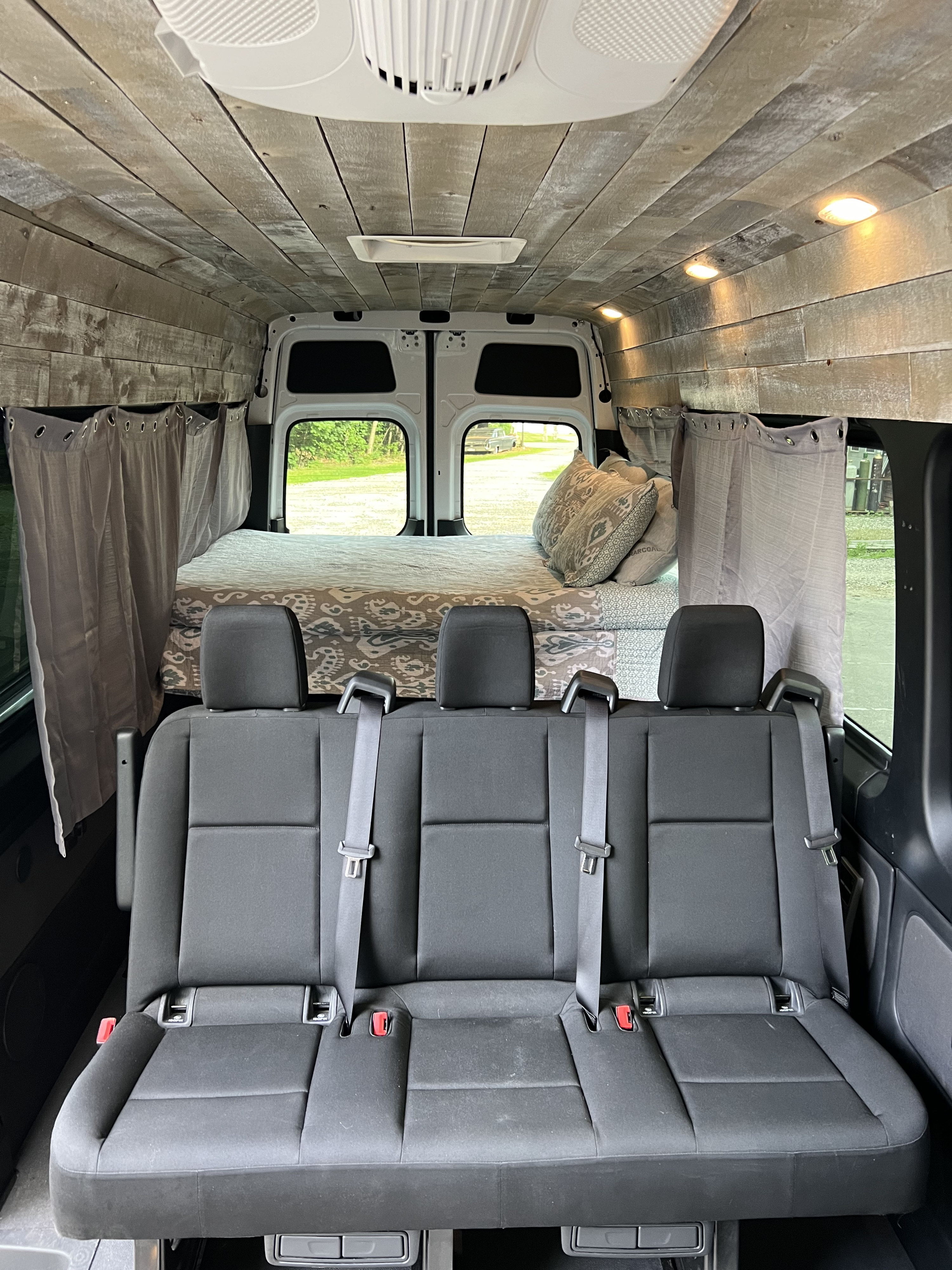 Spacious rv rental interior: custom wood-paneled camper van with rear bed & 3-person seating.. Mercedes-Benz sprinter 2019