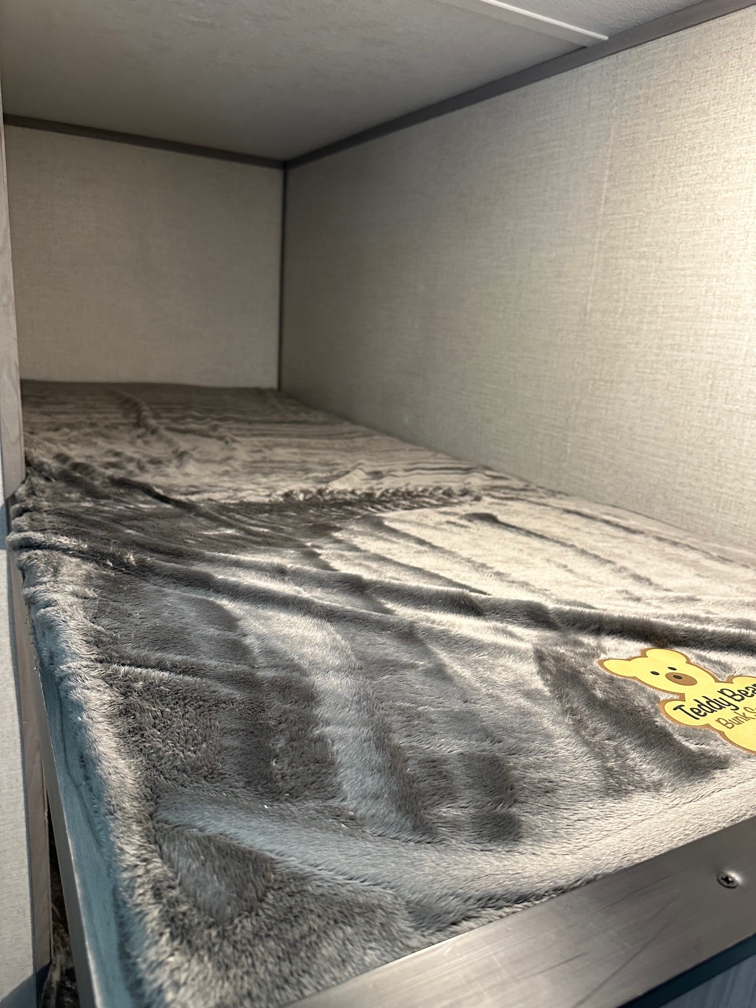 Cozy RV rental bunk bed with soft grey blanket and "Teddy Bear Bunk" label, ideal for compact travel comfort.. Coleman Lantern LT 17 B 2023