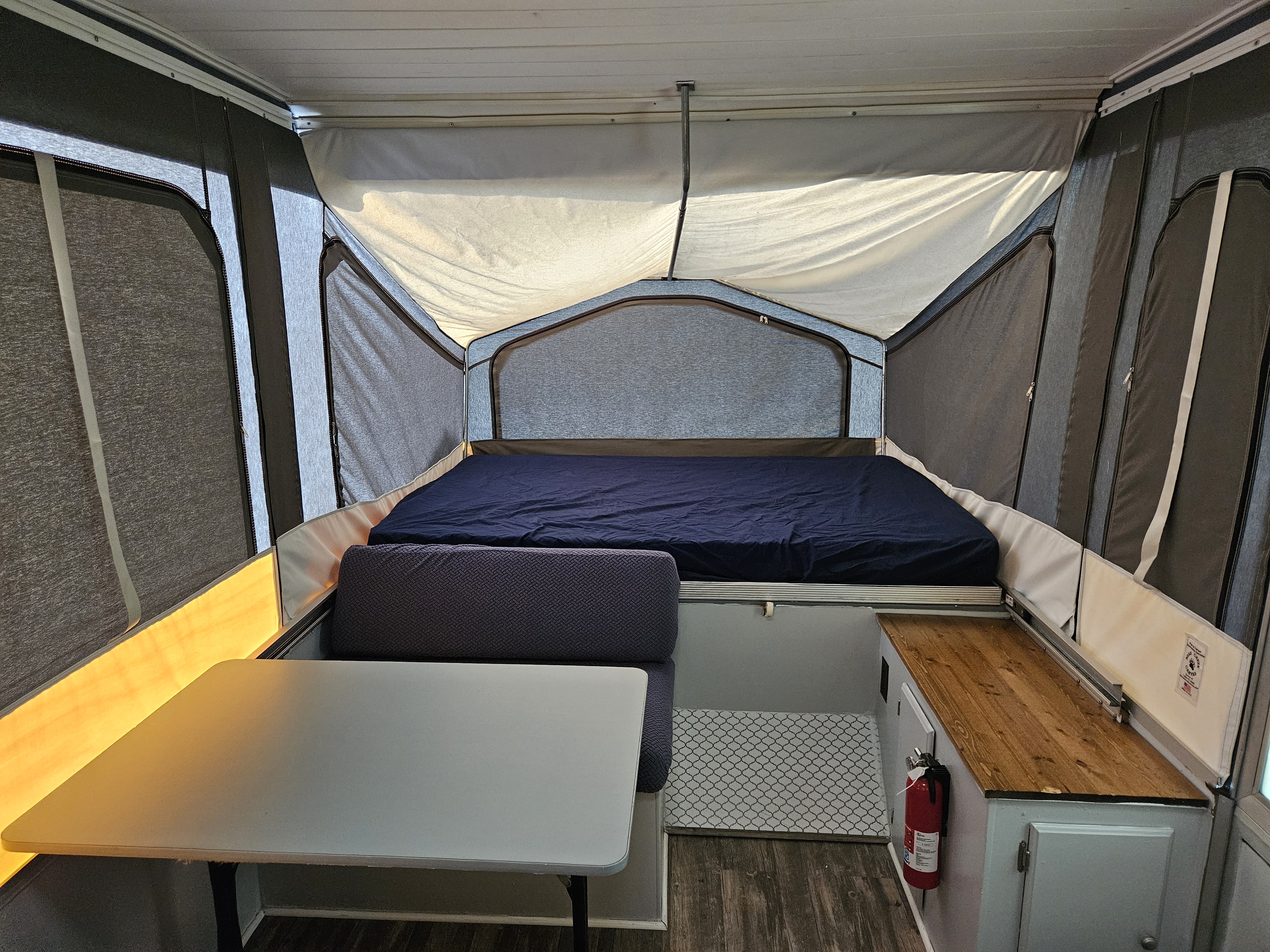 Inside a pop-up RV rental, showing the bed, dinette with table, and compact kitchen area.. Forest River Rockwood Freedom 1994