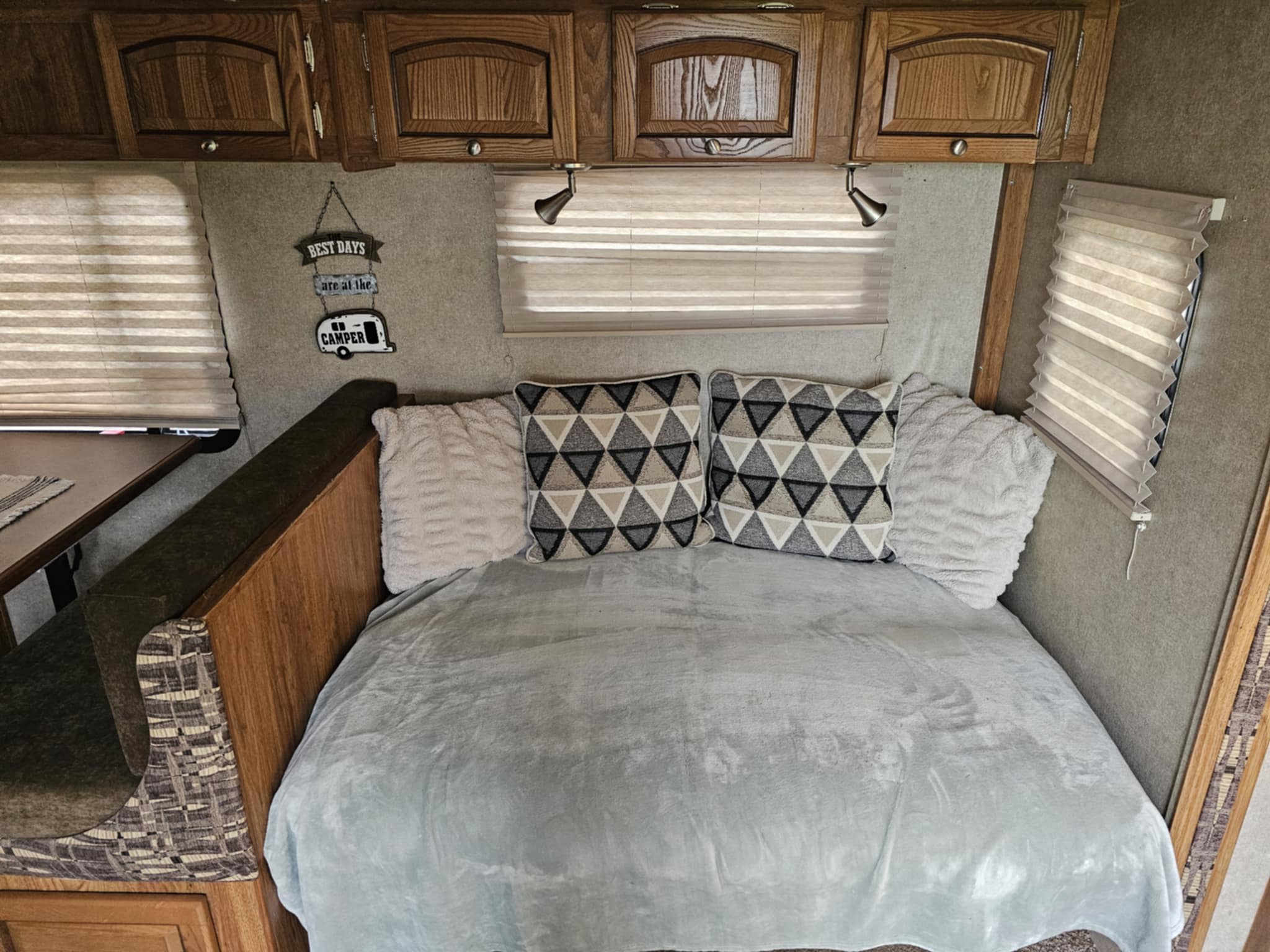 An RV rental's cozy interior, featuring a bed with patterned pillows, wooden cabinets, and windows with blinds.. Forest River Rockwood Roo 2014