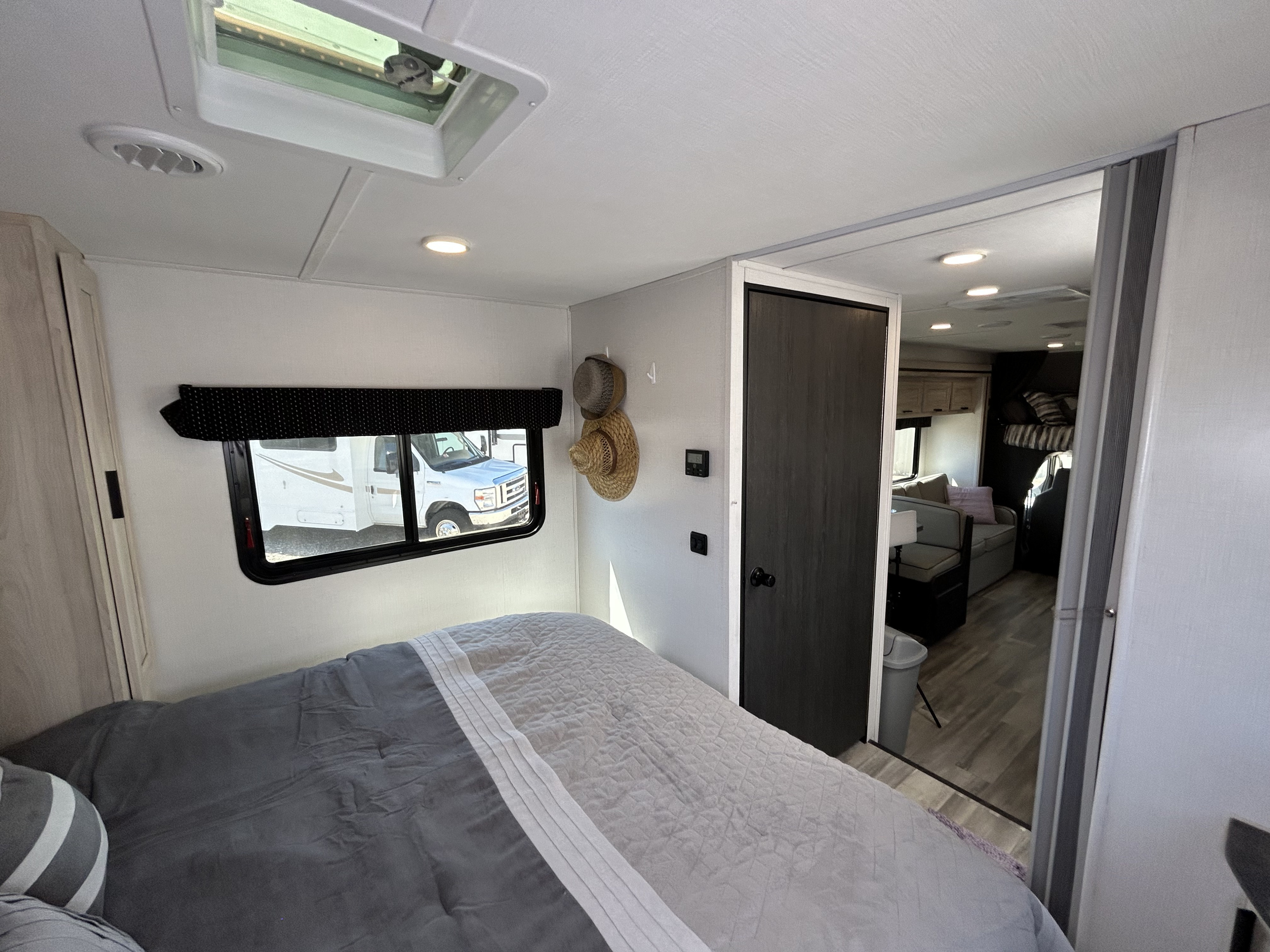 This RV rental's cozy bedroom features a window, a comfortable bed, and a doorway leading to the living area with a sofa and bunk.. Forester LE 2023