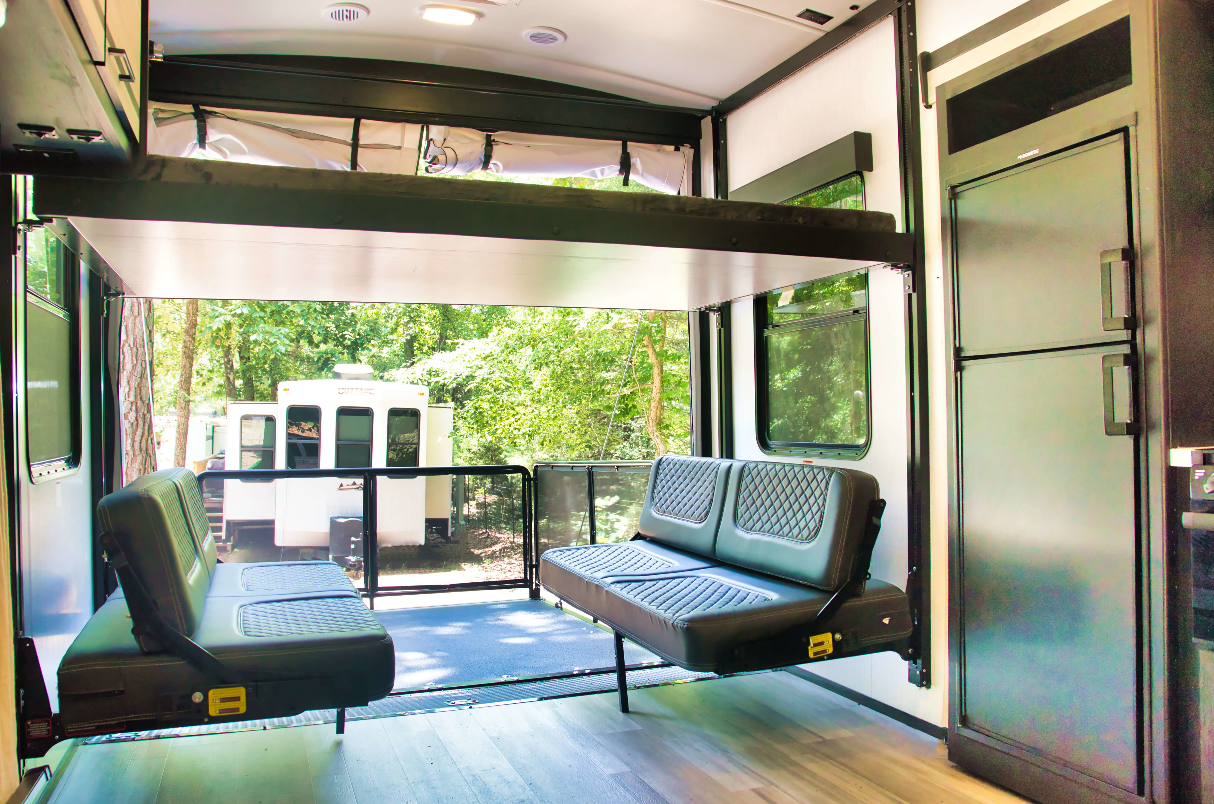 Versatile RV rental interior: Toy hauler garage with fold-down bunk bed, seating, and an open patio overlooking nature.. Cruiser Stryker 2022