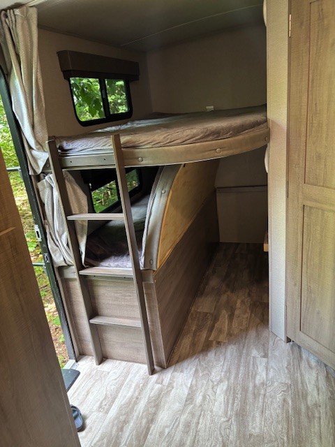 RV rental interior: light wood-look flooring and cabinetry, bunk beds with mattresses, a ladder, and nature views from windows.. Grand Design Imagine 2020