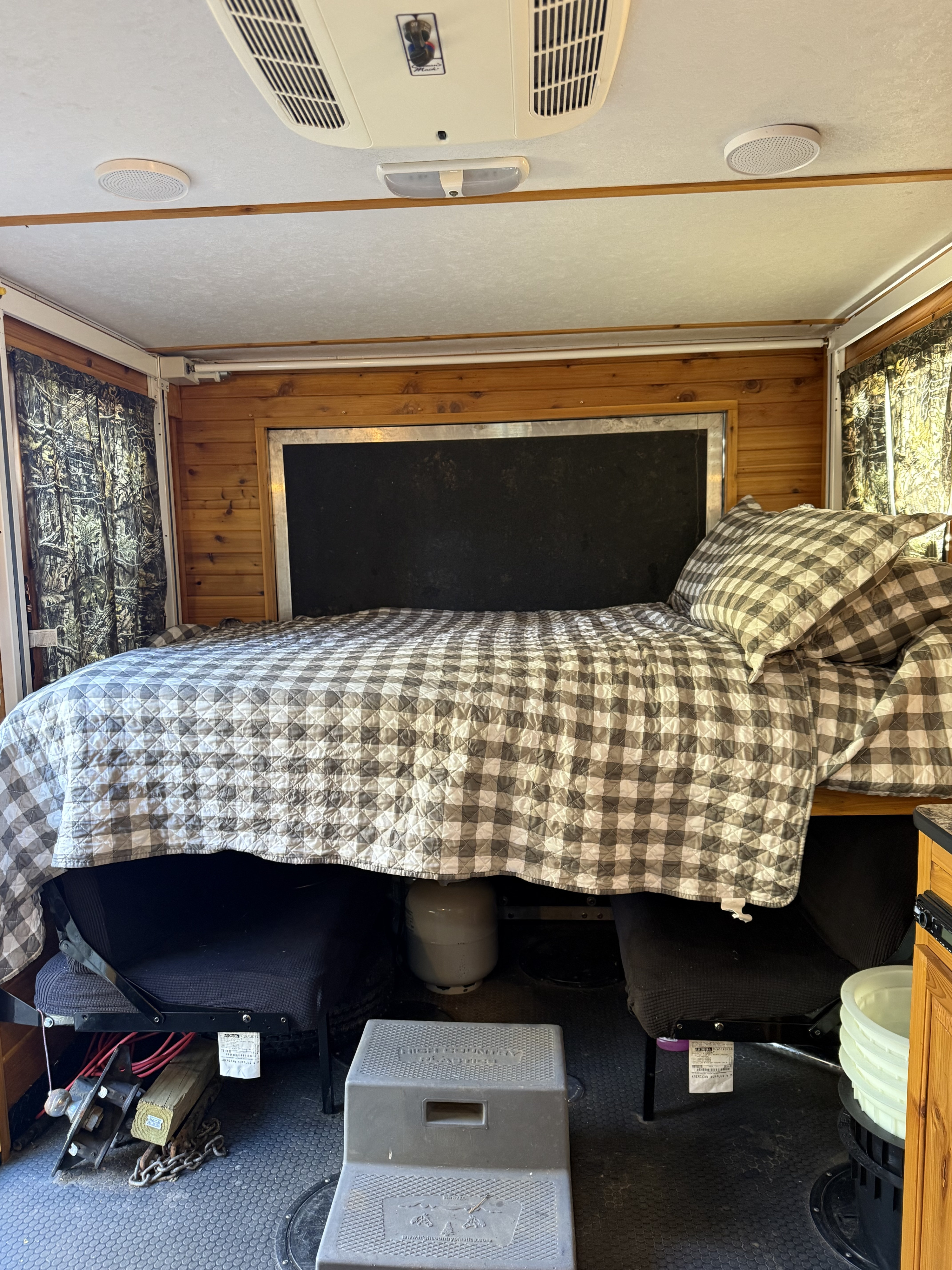 RV rental interior: a checkered bed, overhead AC, wood paneling, and floor seating with a propane tank.. Ice Castle Fish Houses Toy Hauler 2016