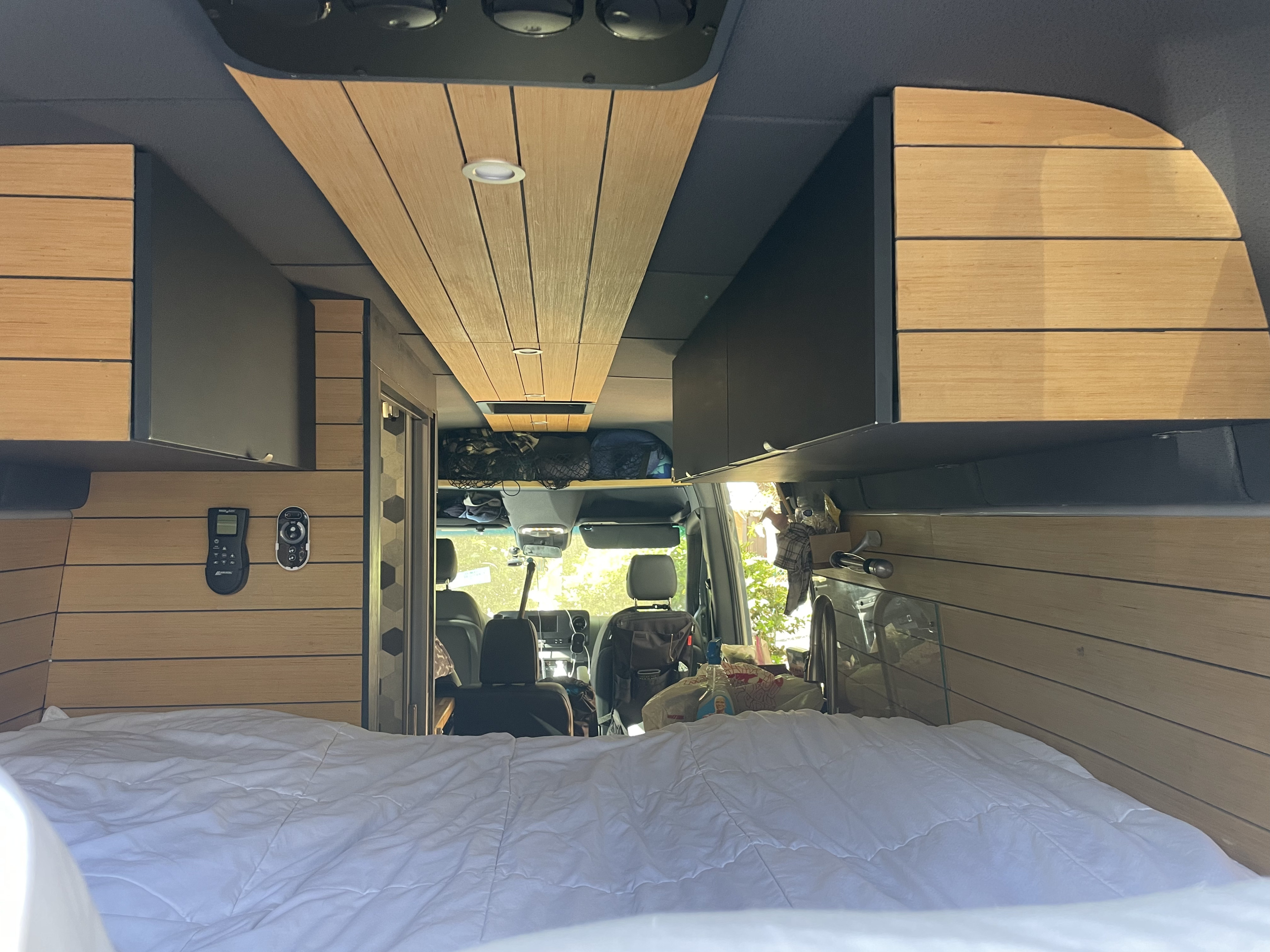 View from the bed of a spacious RV rental, featuring sleek wood paneling, storage cabinets, and front cockpit.. Mercedes Benz Sprinter 2500 4x4 Off Grid Conversion 2020